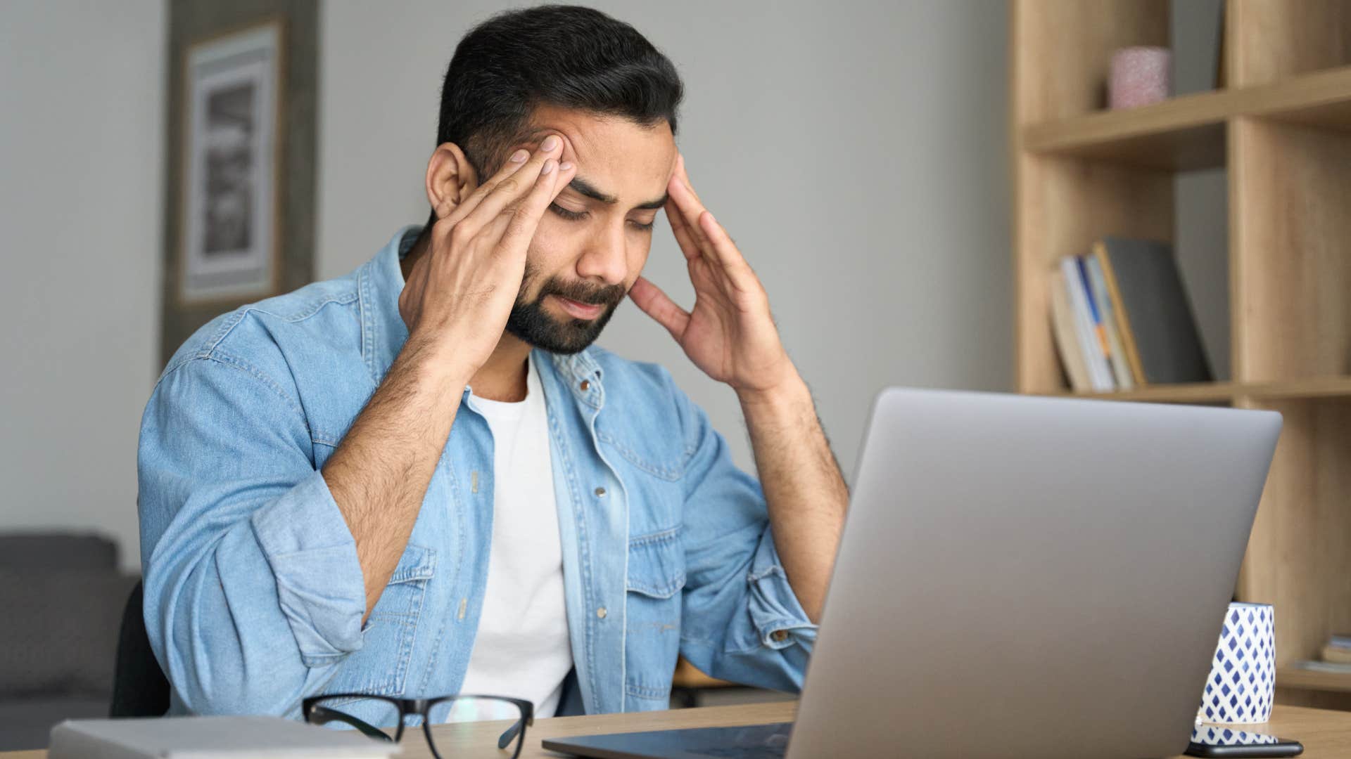 Stressed man holding his forehead in front of his laptop