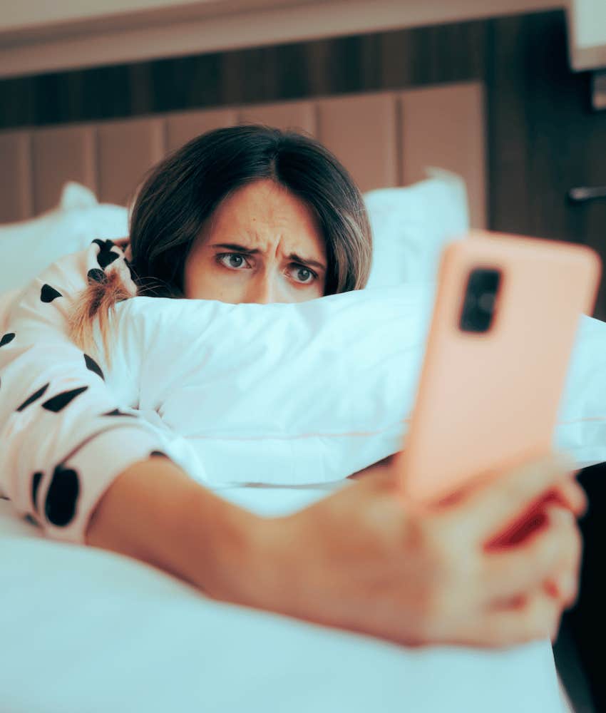 Woman hides behind pillow while checking mobile phone for red flags