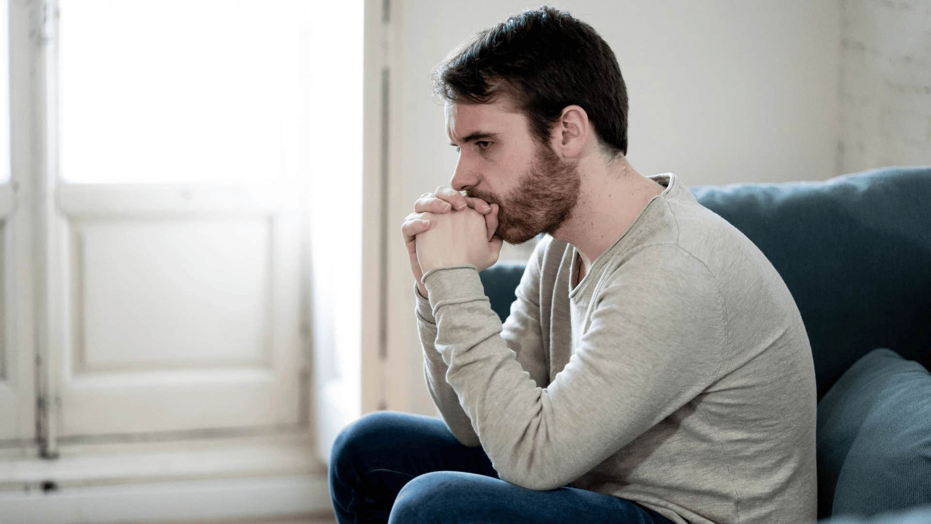 upset man sitting on couch haunted by regrets that destroyed his marriage