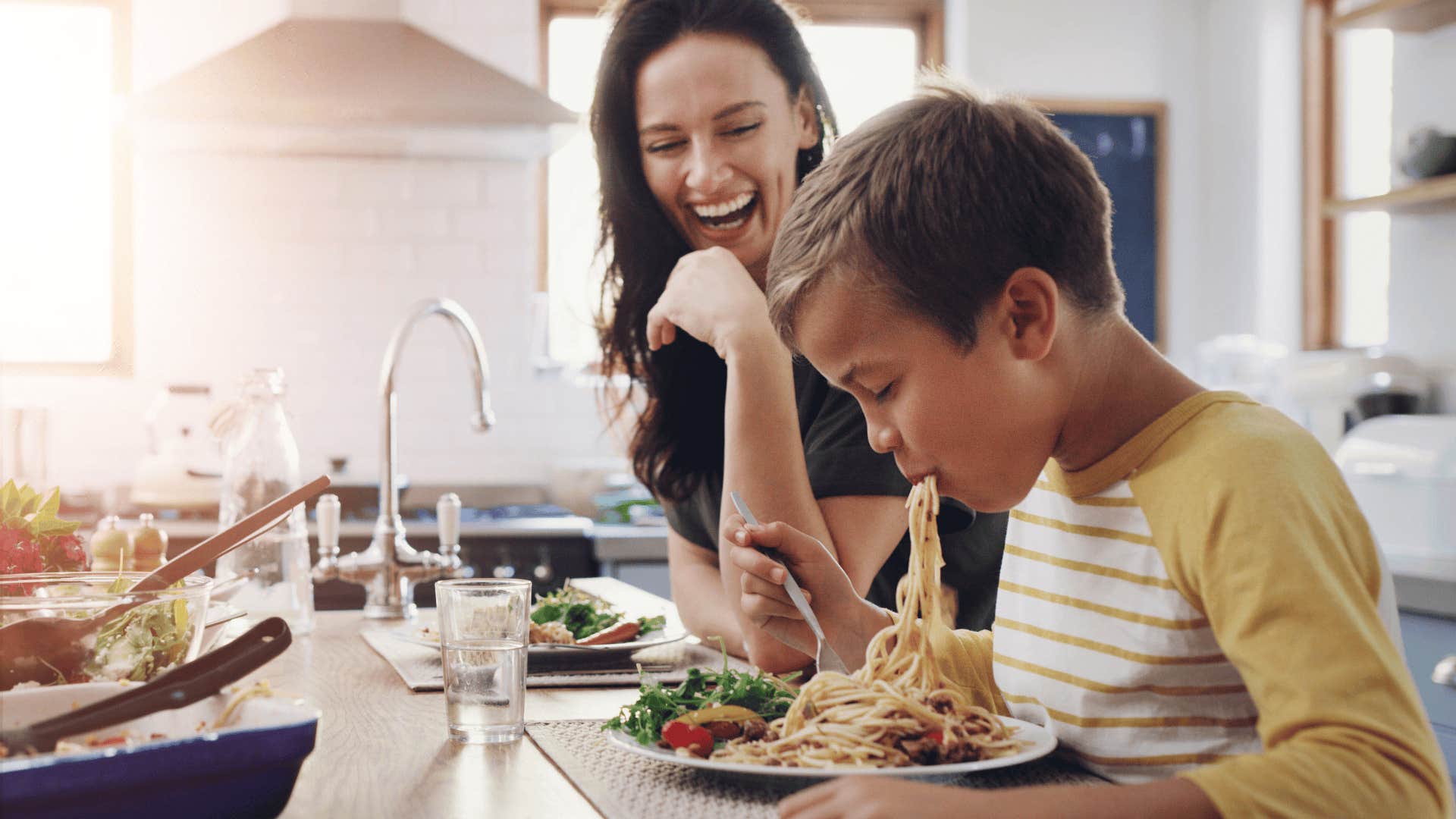 woman laughing at her young son eating spaghetti
