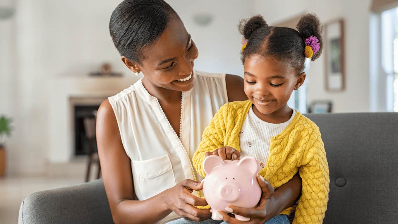 Smiling woman holding a piggy bank and her young daughter on her lap.
