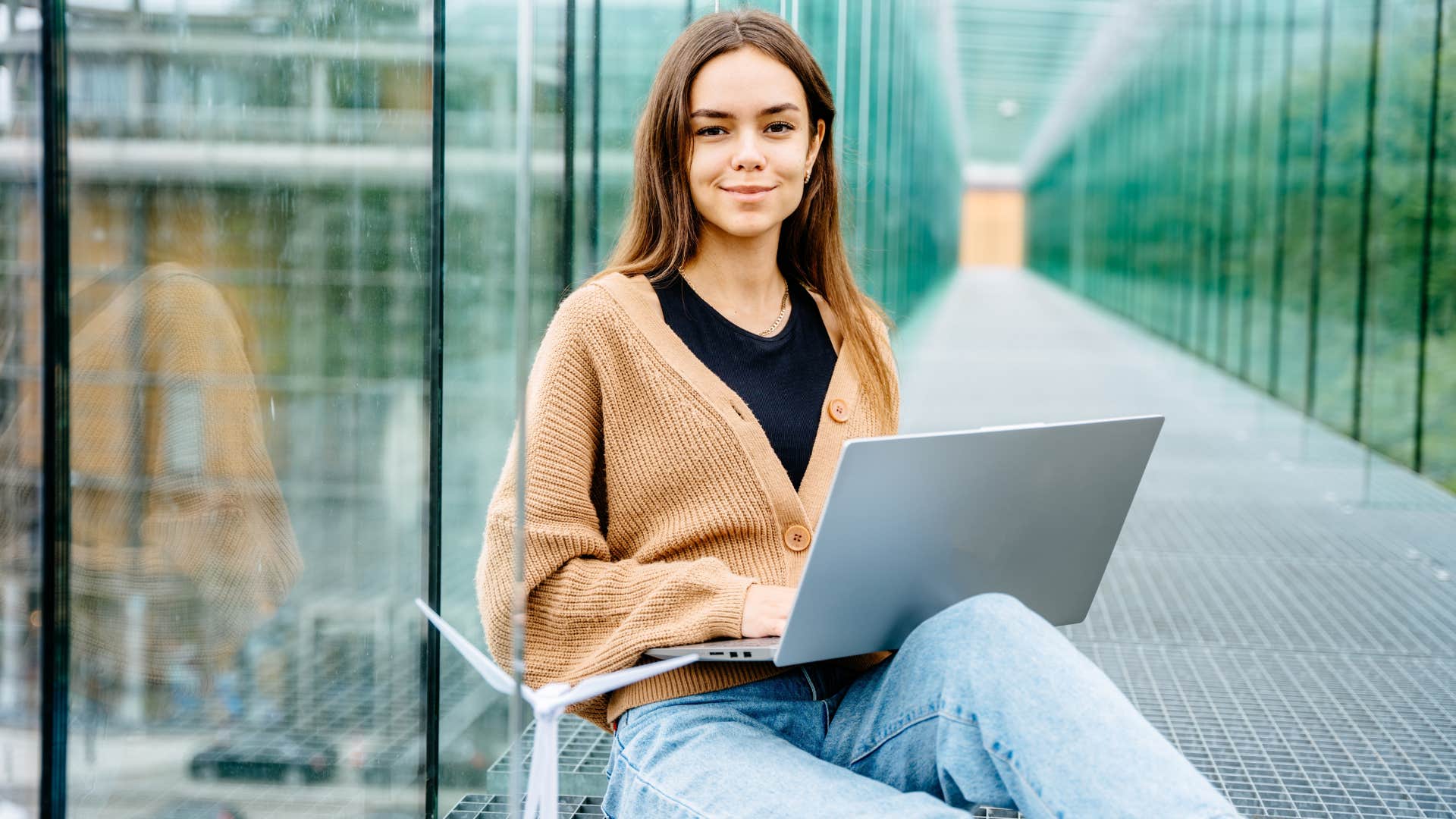 gen z woman on laptop in work hallway
