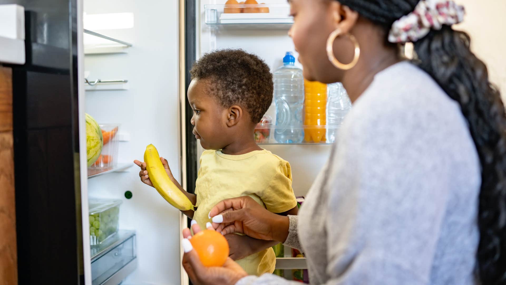 Woman helping her young son put away groceries in the refrigerator
