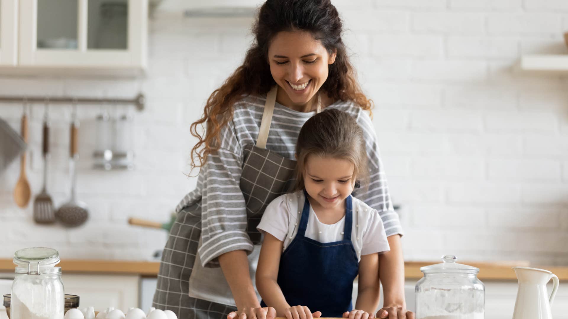 Nanny smiling and helping a young girl bake