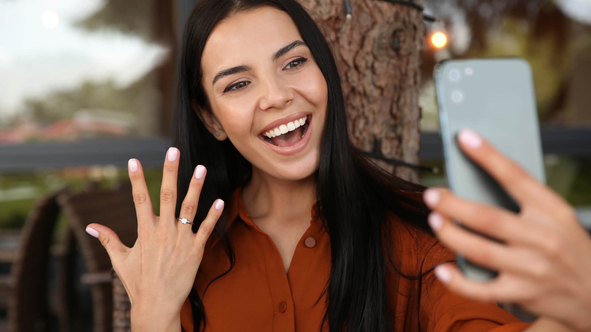 Millennial woman smiling and holding up her hand with a diamond ring on