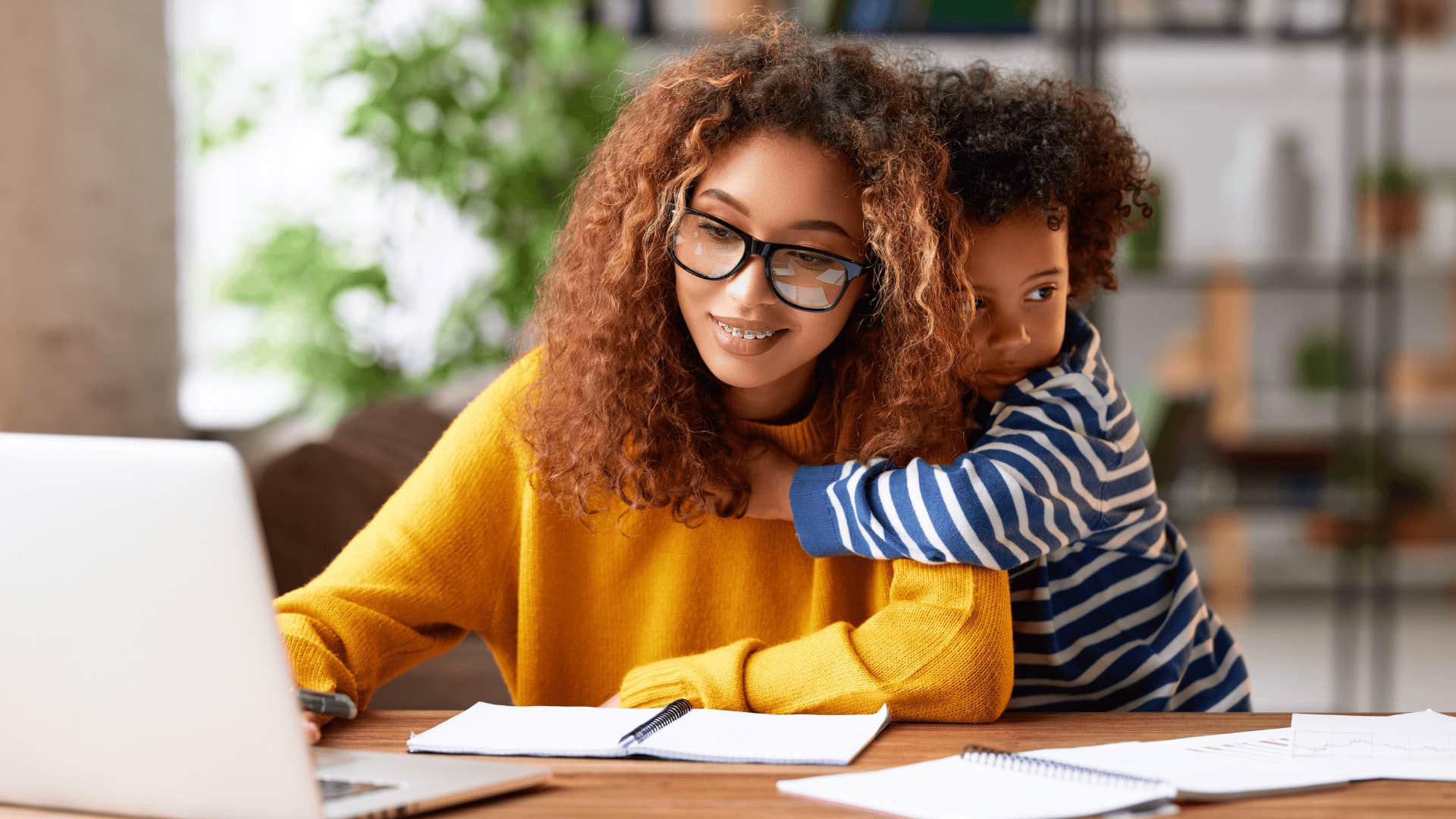 young mother doing homework with child hugging her