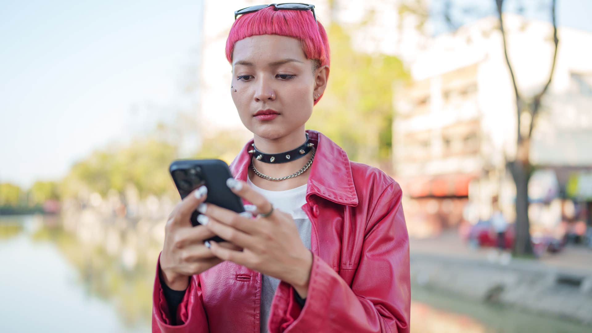 young person with pink hair texting on her phone