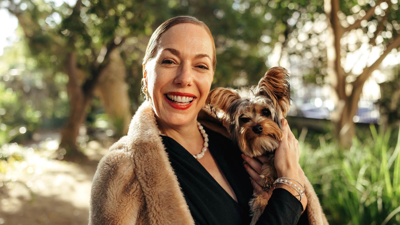 Things Wealthy People Refuse To Do That The Middle Class Keeps Saying Yes To wealthy woman holding a dog and smiling