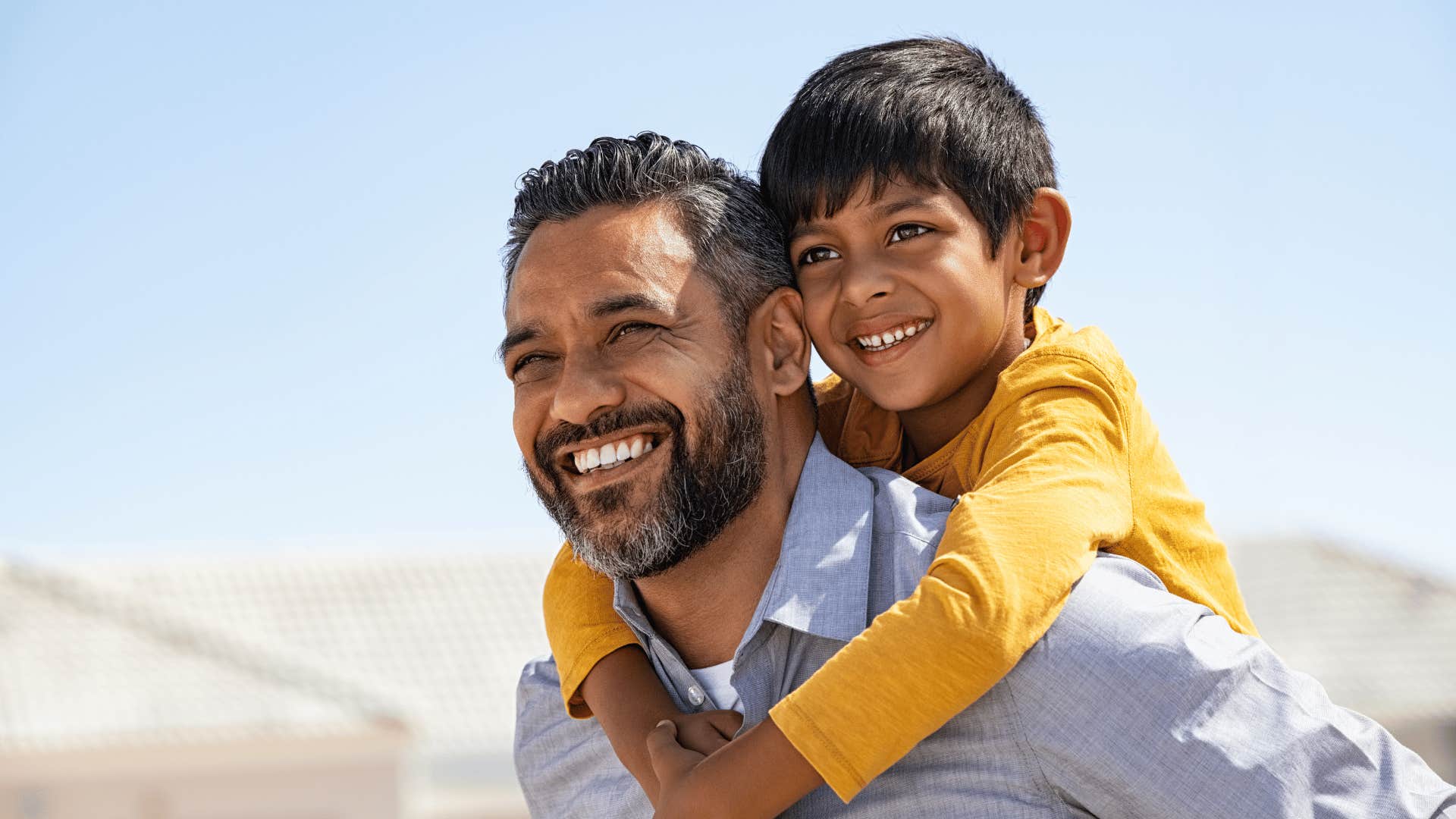 Happy man carries child on shoulders to mirror his childhood