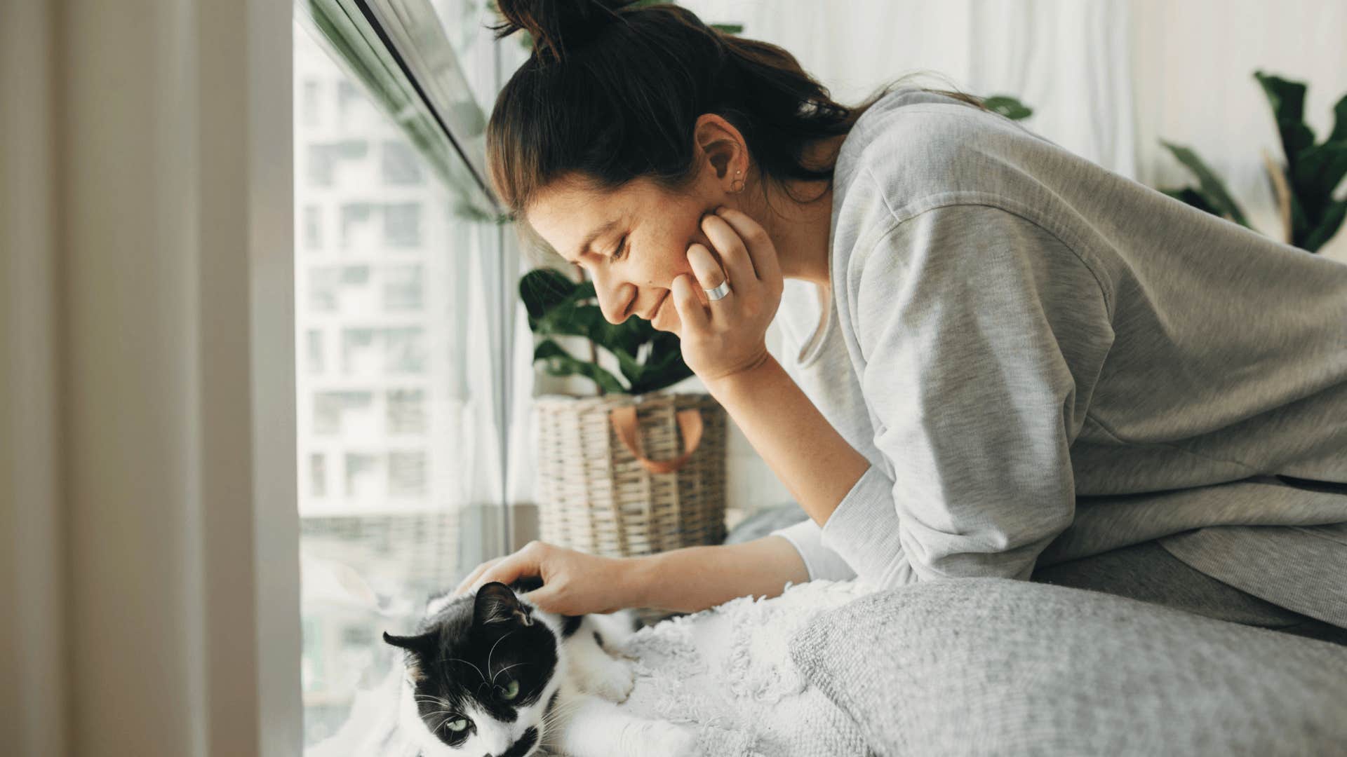 gen z woman smiling and petting her cat in it's own bedroom