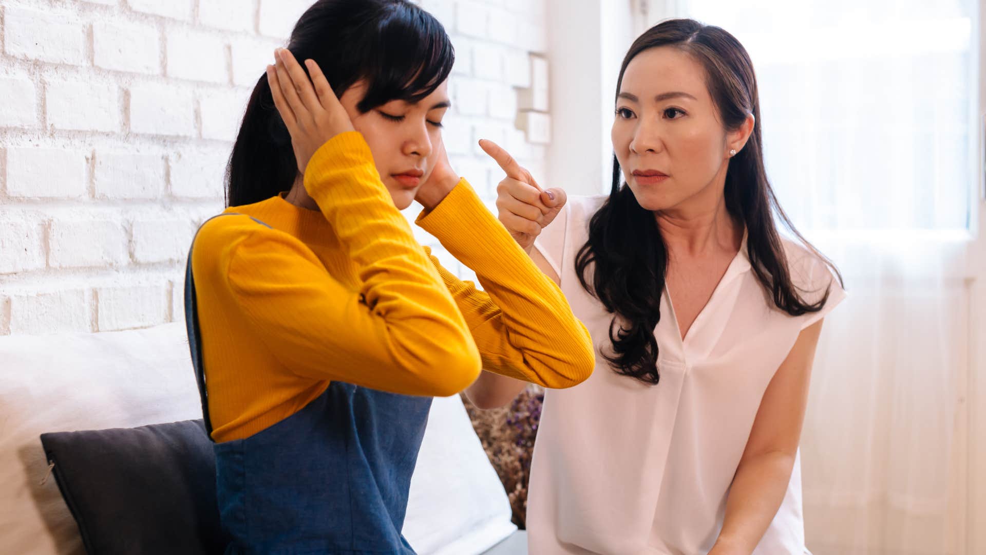 young woman covering her ears while her mom guilt-trips her