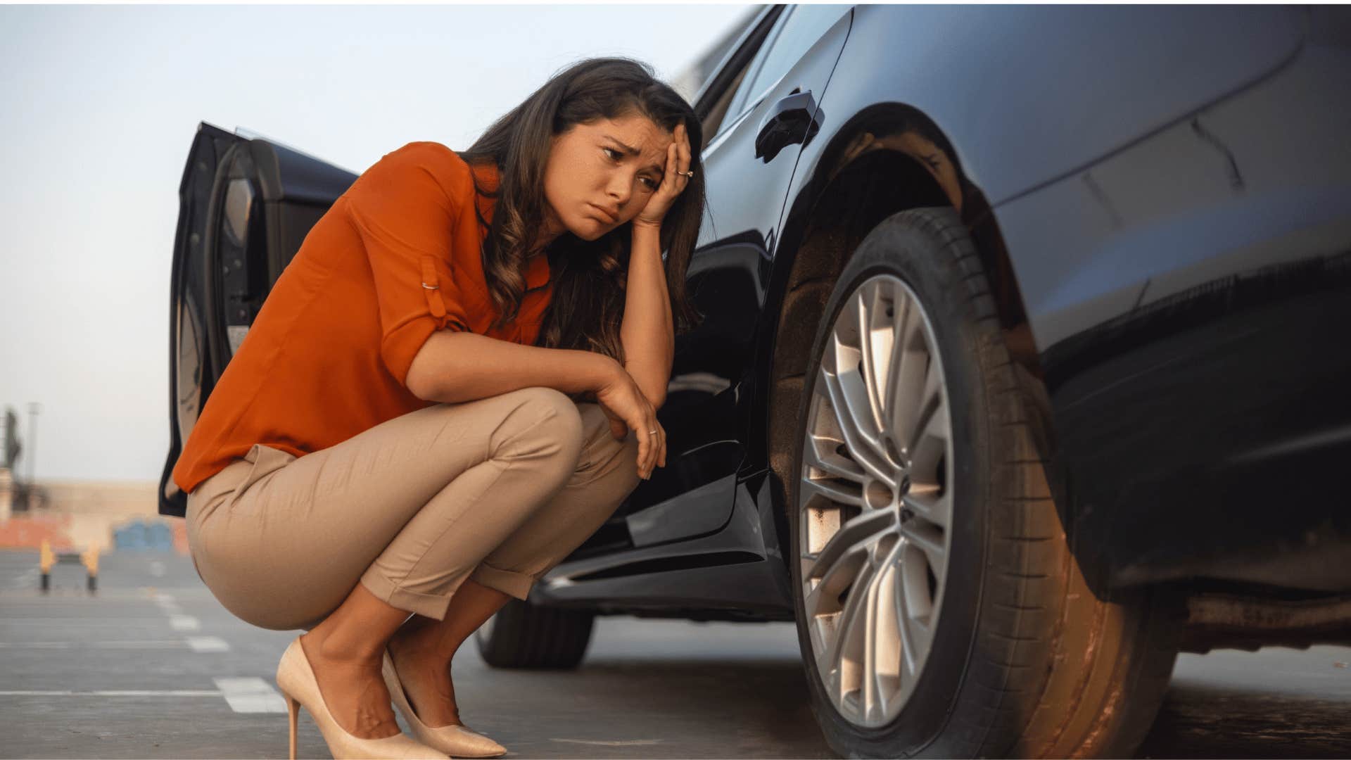 stressed woman looking at deflated tire at gas station