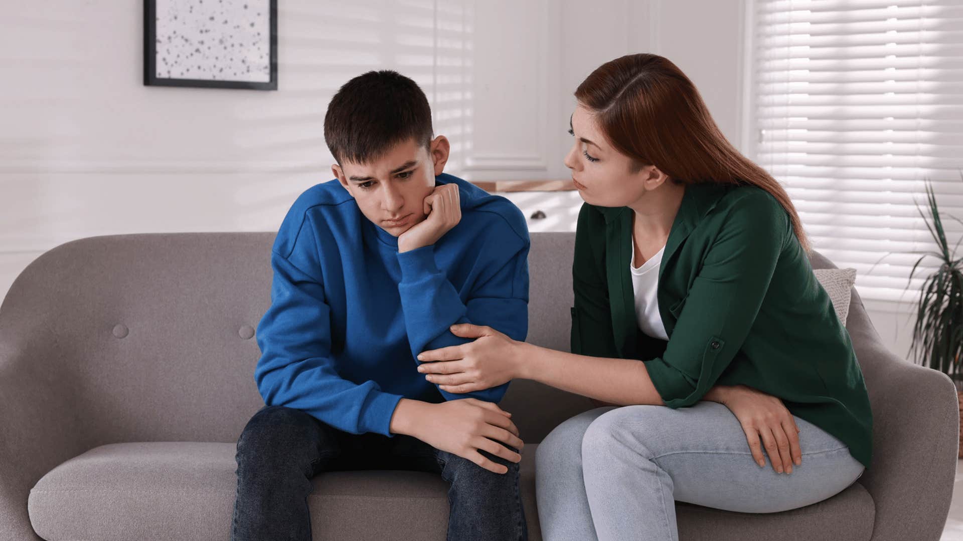mother sitting on the couch with her son asking him are you sure you’re okay