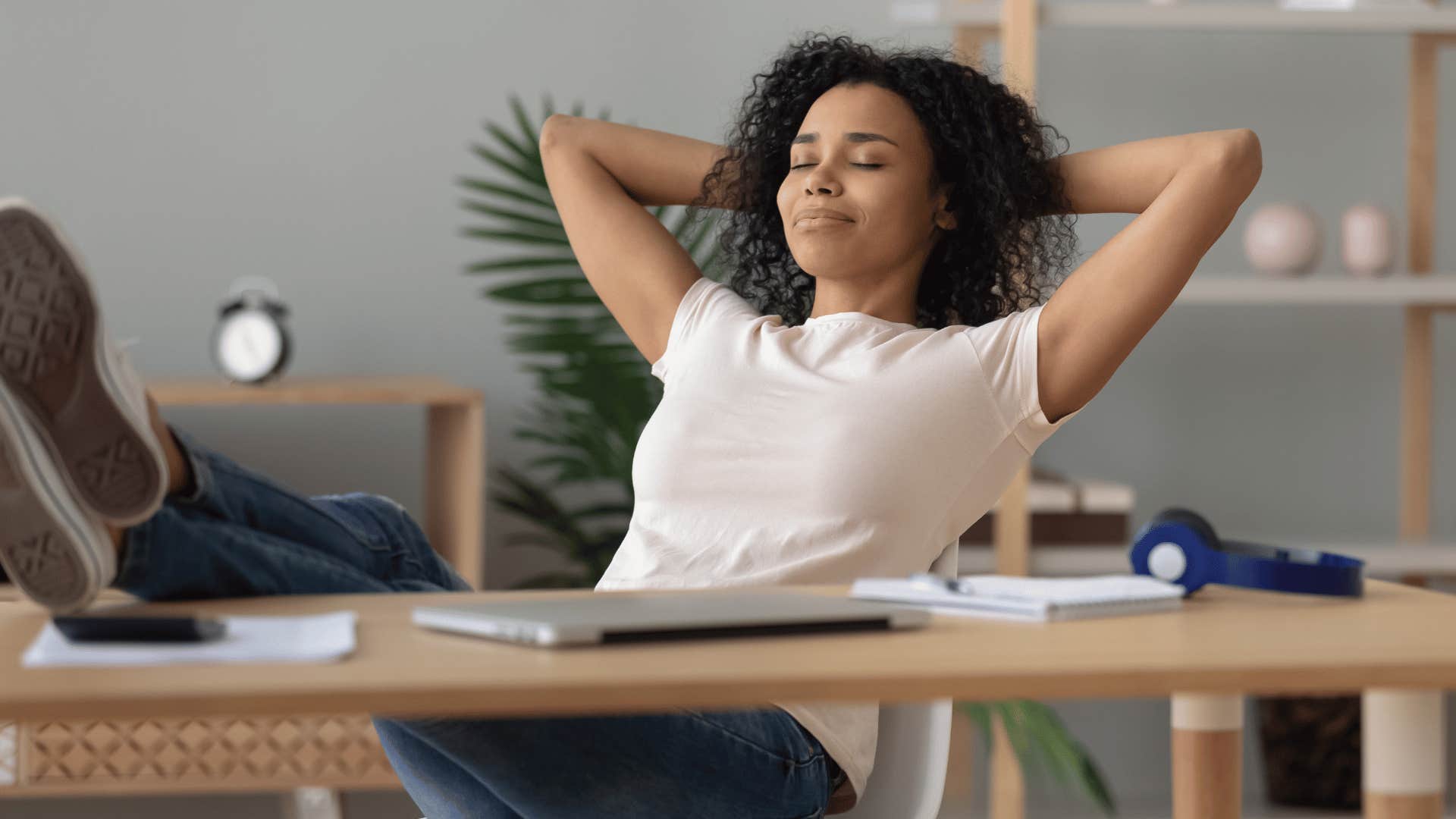 woman in white shirt throwing legs up on wooden desk as she keeps her cool
