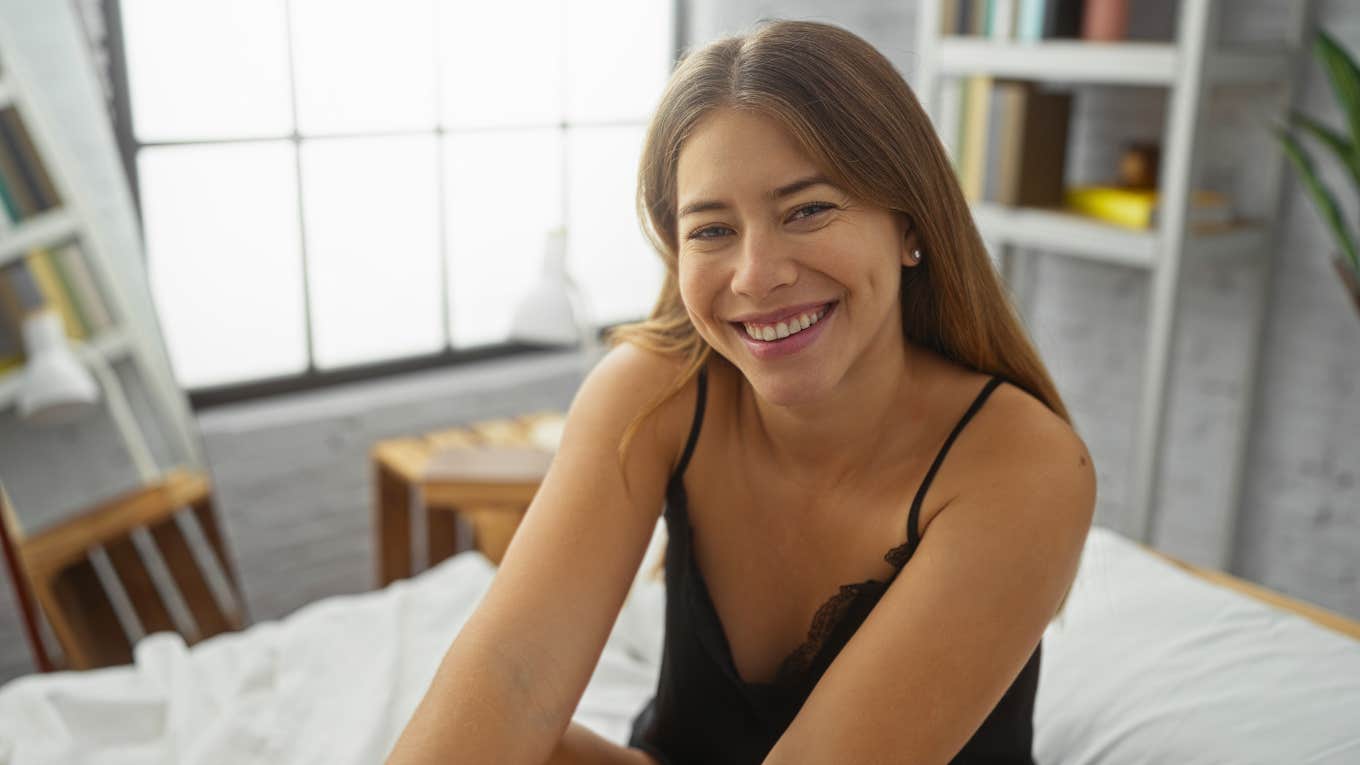 Big Tariff Energy Is Coming For Your Bedroom Fun — Stock Up On Adam & Eve Toys While You Still Can smiling woman sitting in bed about to use adam & eve products