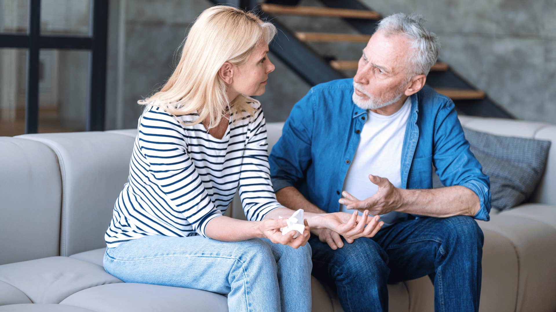 woman in stripped shirt asking for understanding from man in blue shirt on the couch