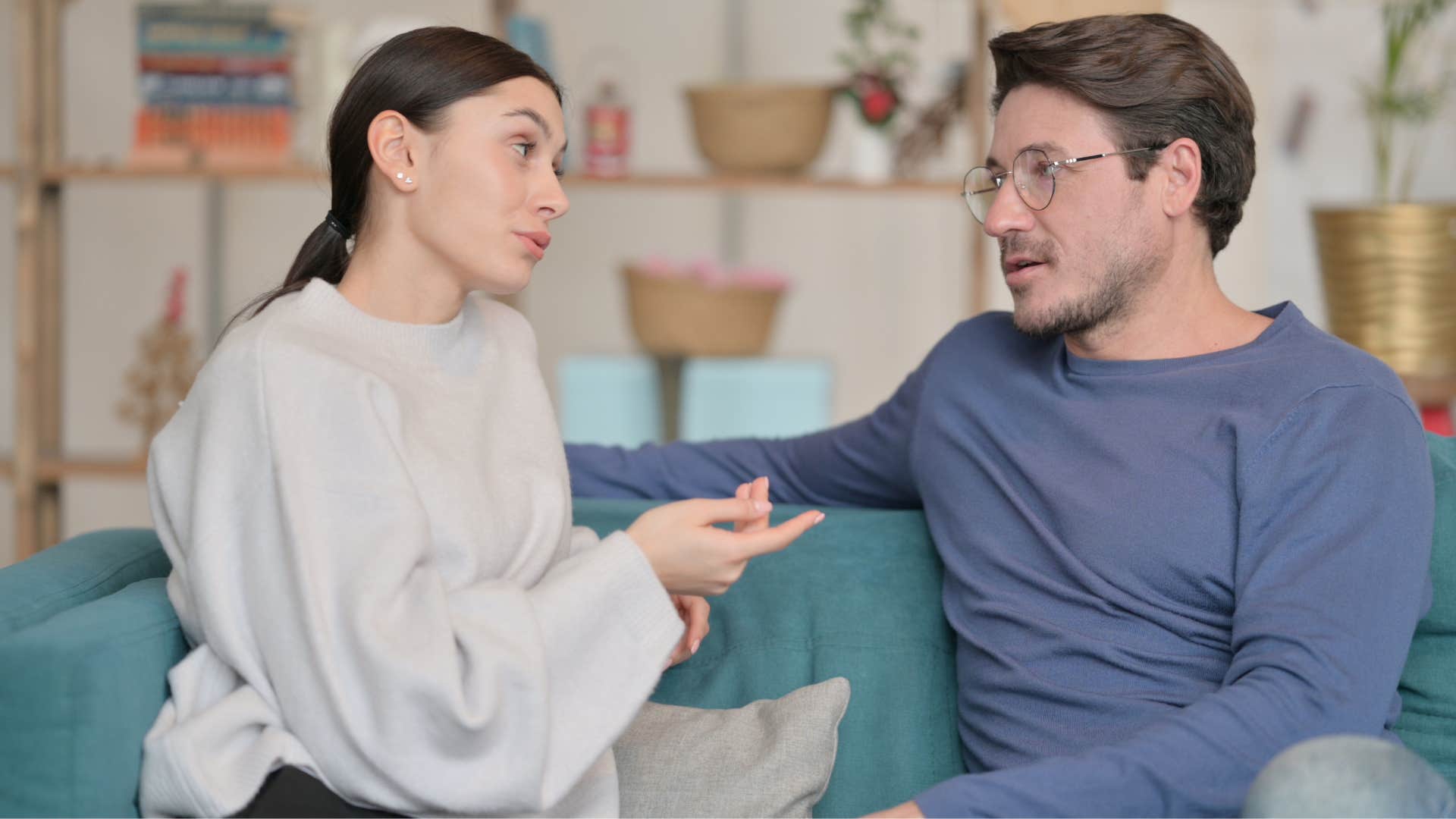 woman asking if it's okay if she leaves early or would that be considered rude to man in blue shirt as they sit on the couch facing one another