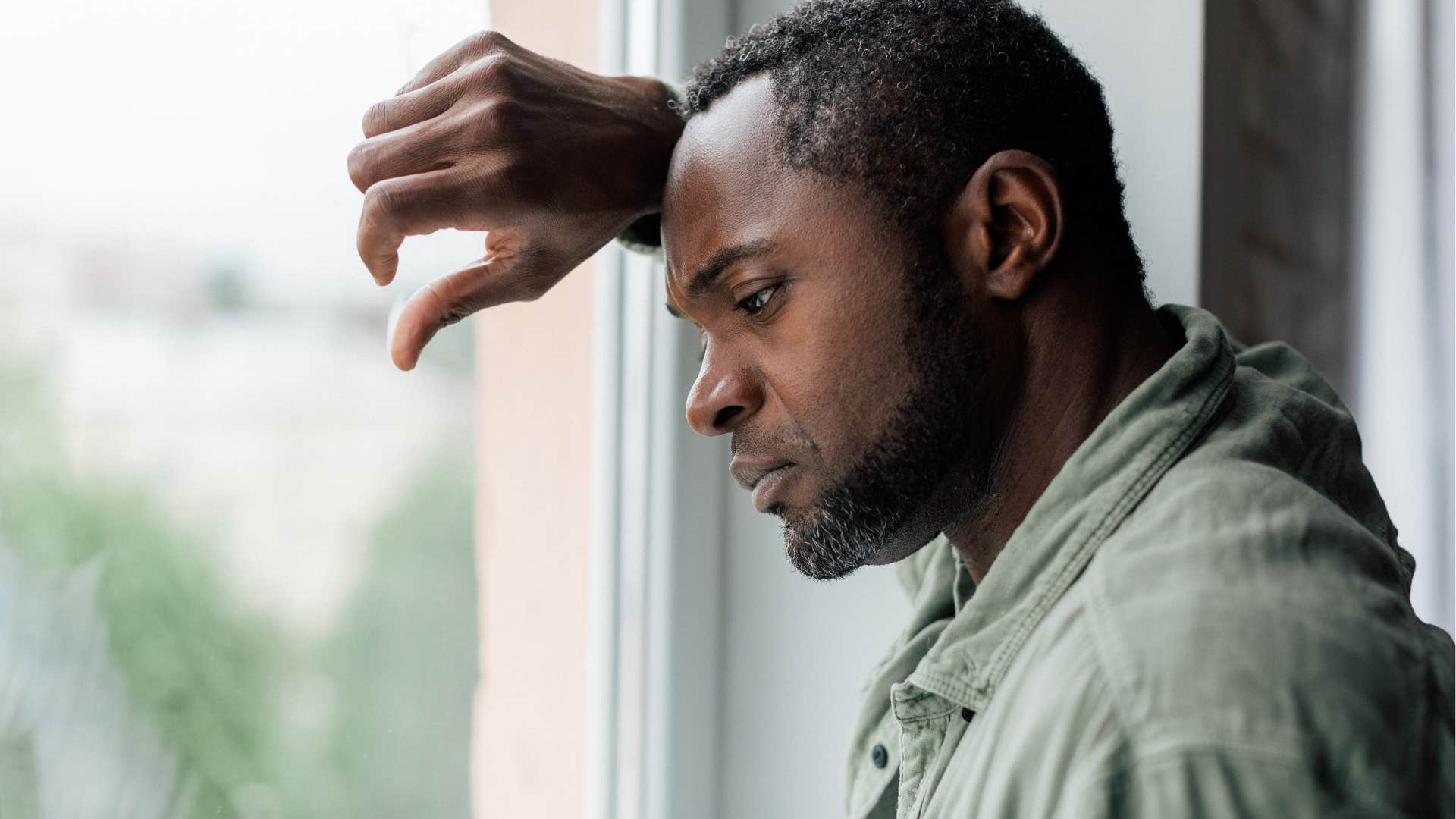 man battling unresolved trauma looking out a window sadly