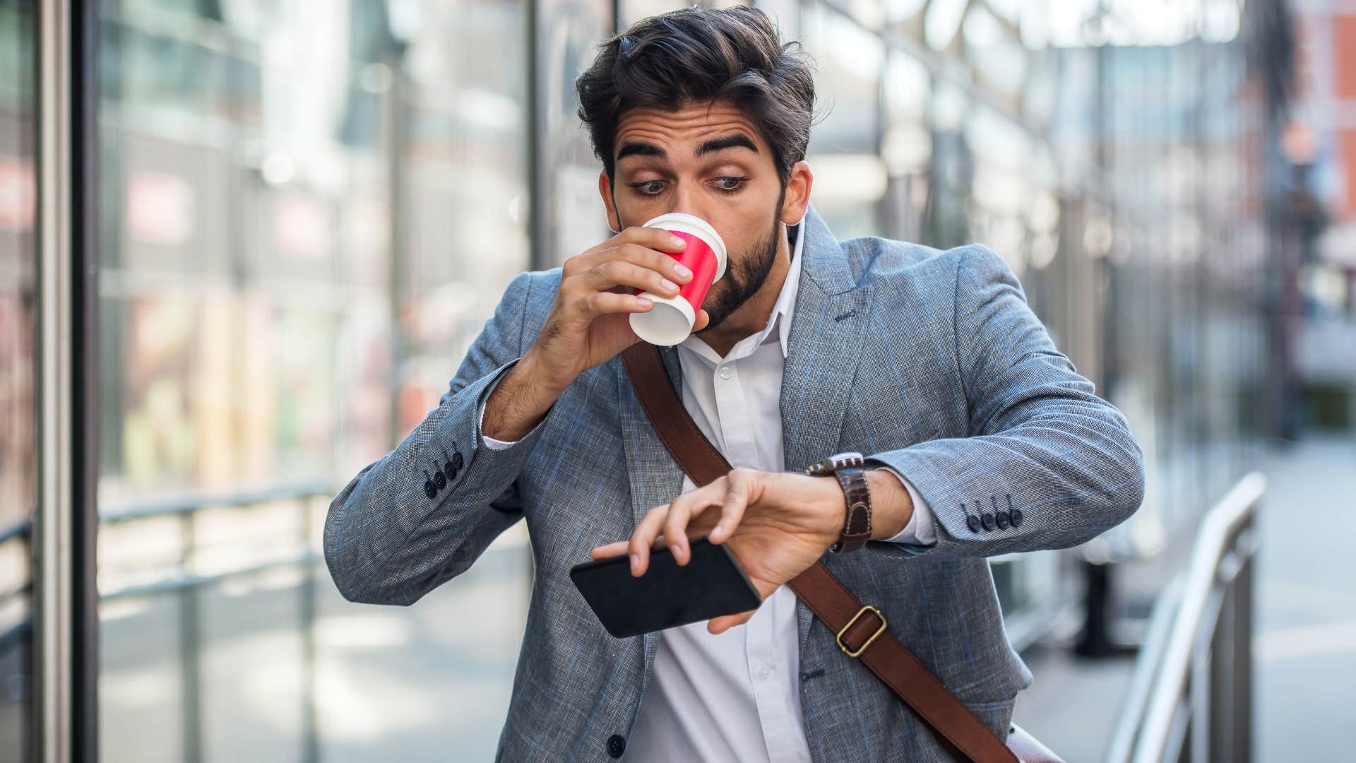 Stressed man maintaining a big workload checking his watch and drinking a coffee.