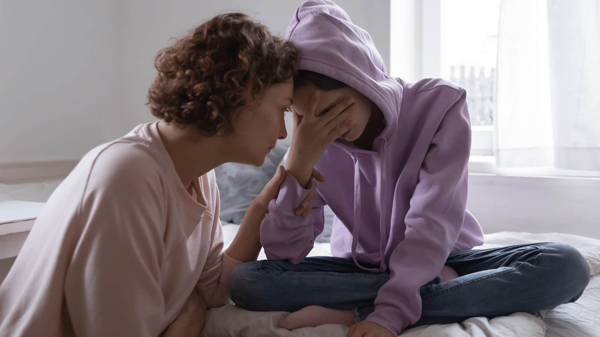 Upset girl turned away from her mom trying to show her affection.
