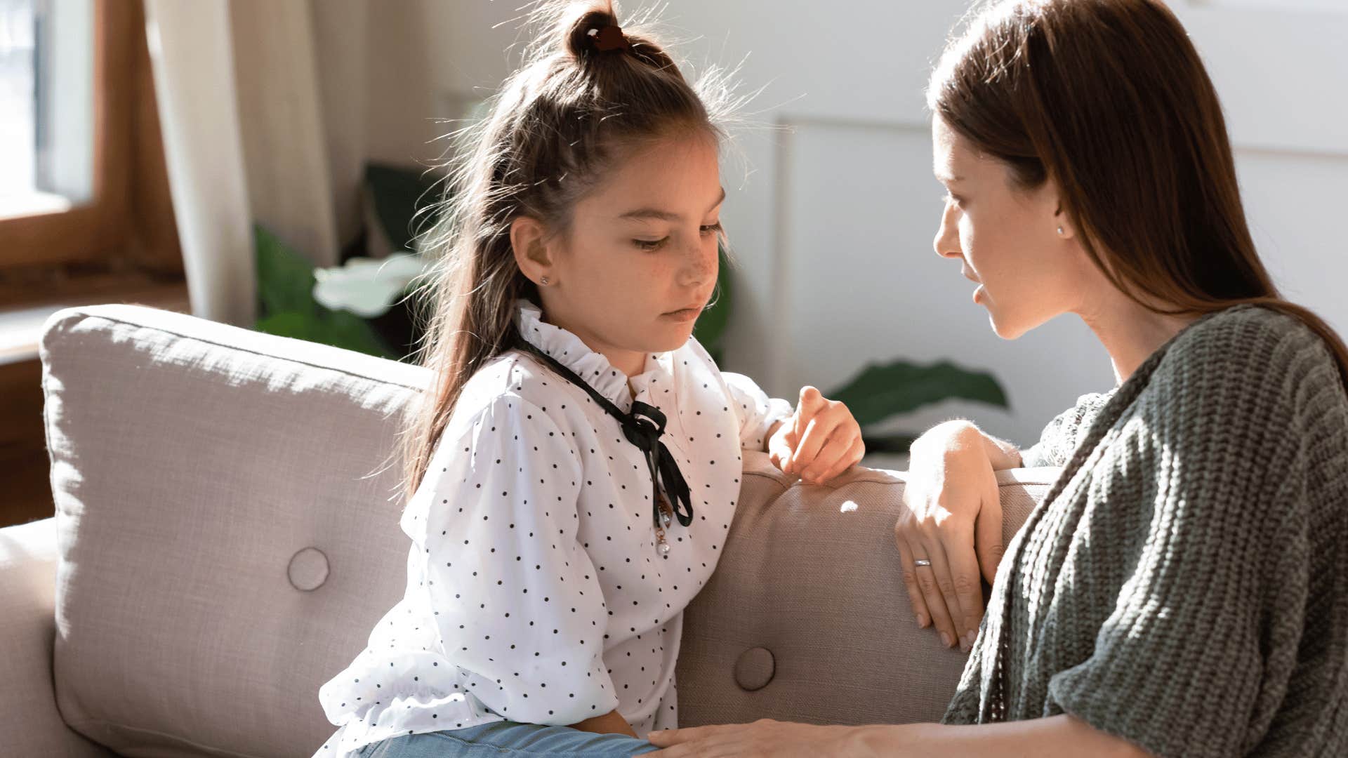 Upset young girl having a family check-in with her mother on a couch.
