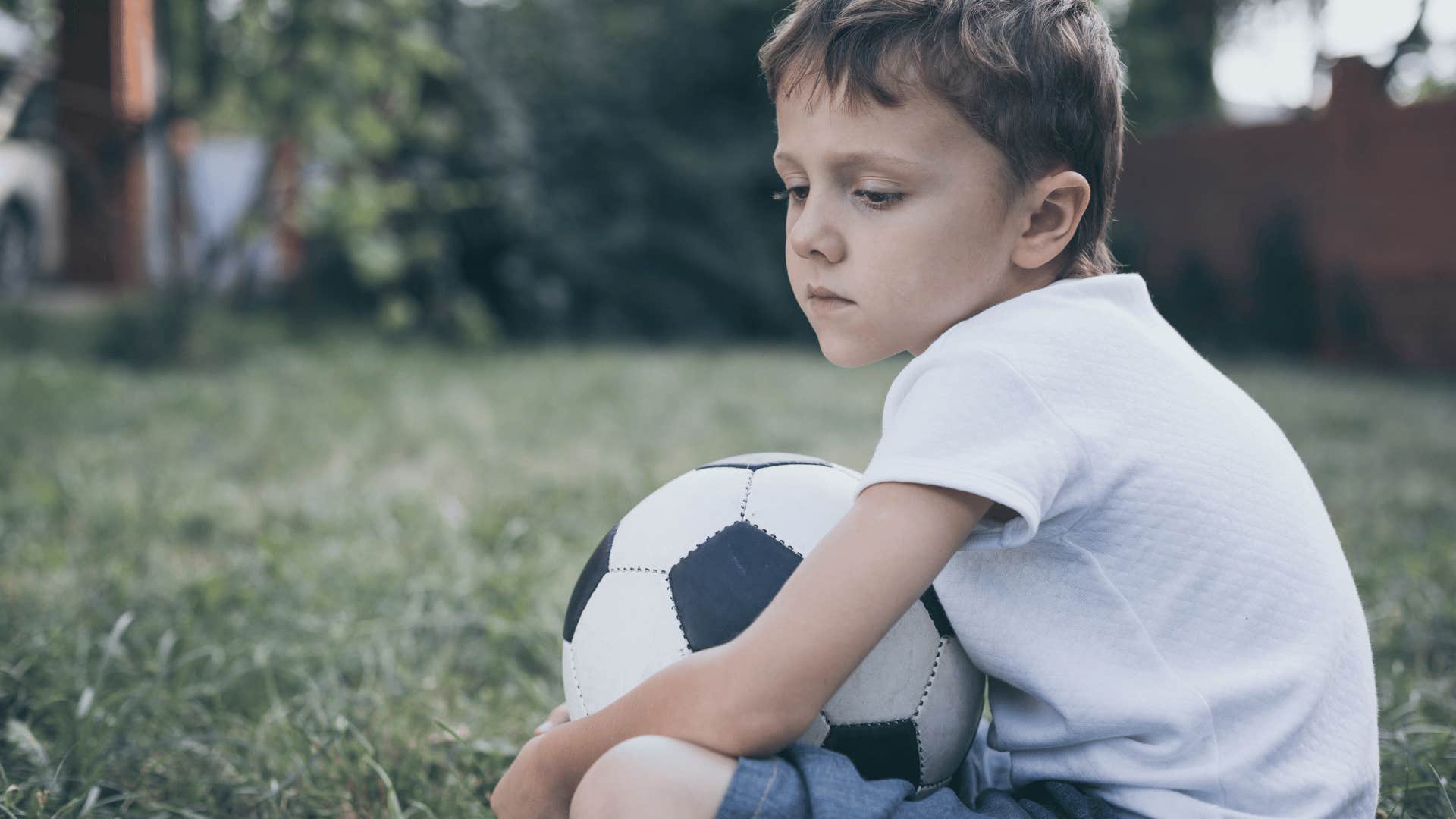 Upset kid sitting with a soccer ball after his parents were making him play a sport.