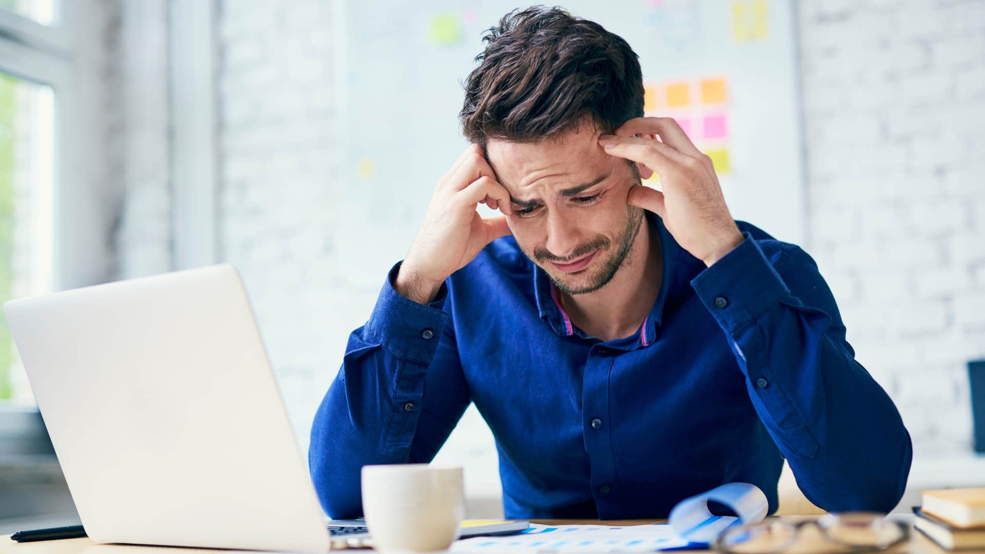 Man who believes emotions are a sign of weakness crying at his desk.