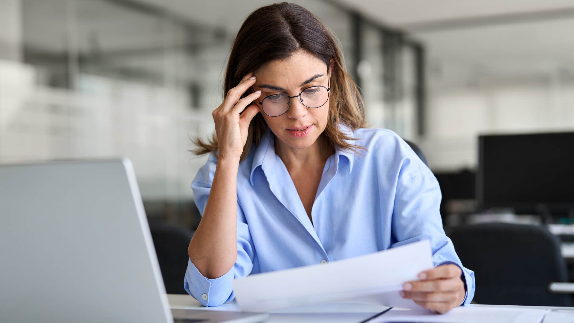 Woman who believes hard work is the key to success holding her forehead at her desk.