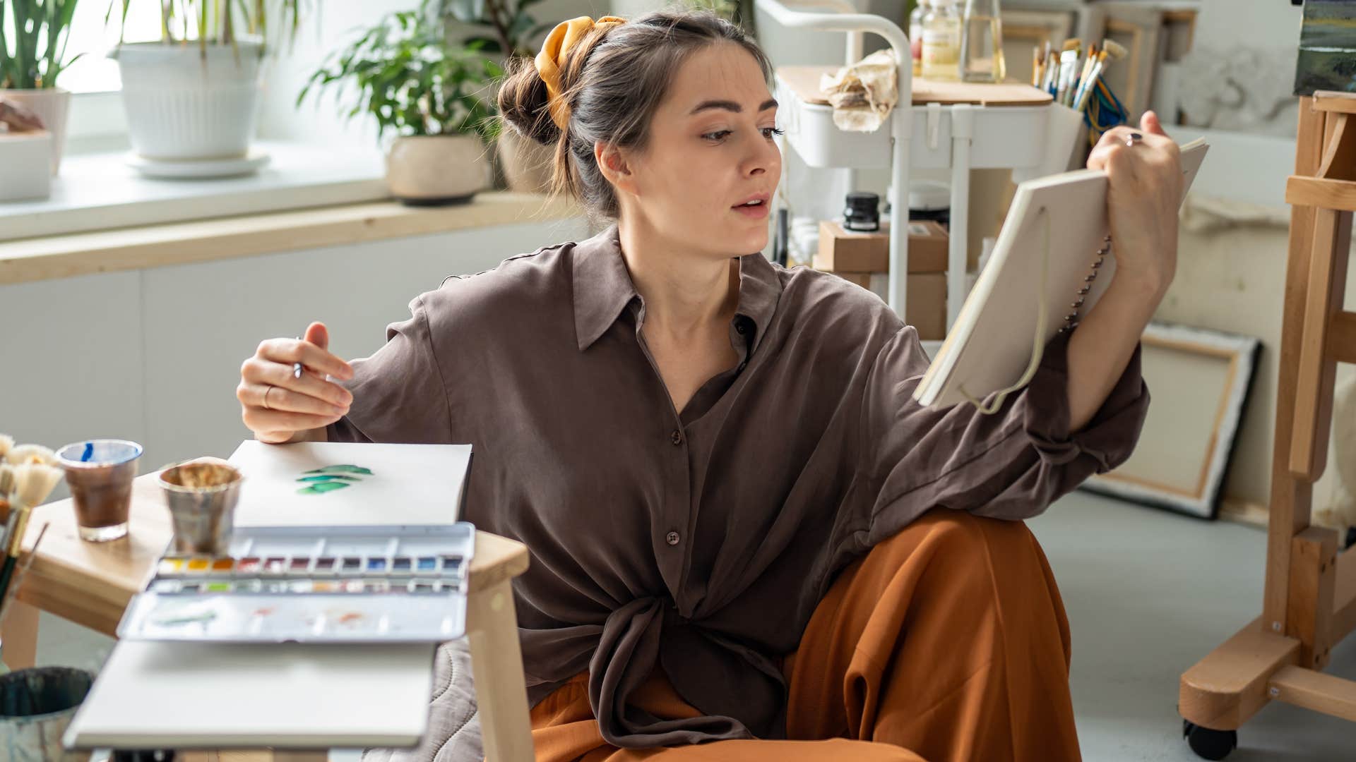 Woman who believes hobbies should be side hustles painting at home.