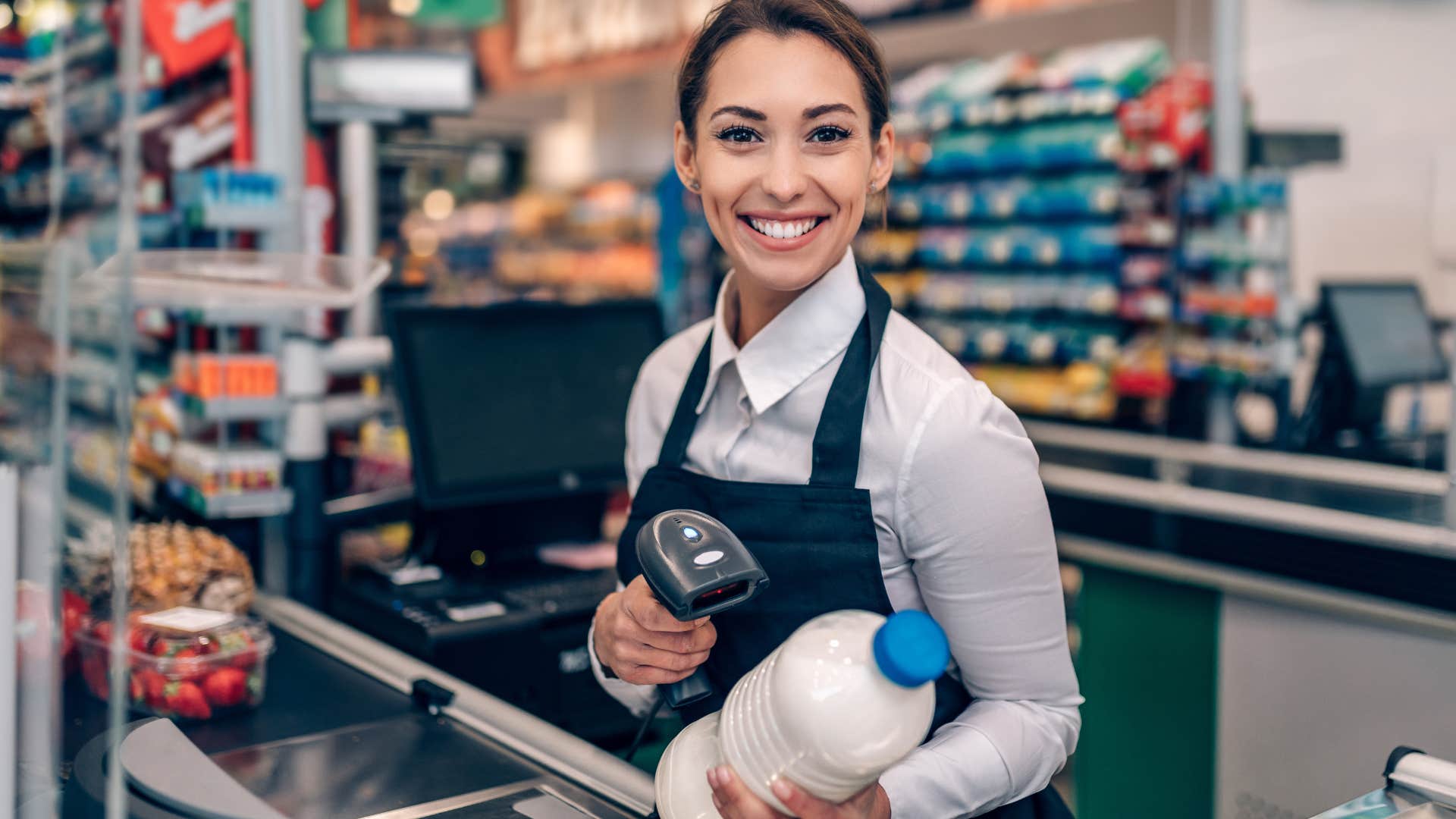 Cashier smiling and holding groceries.