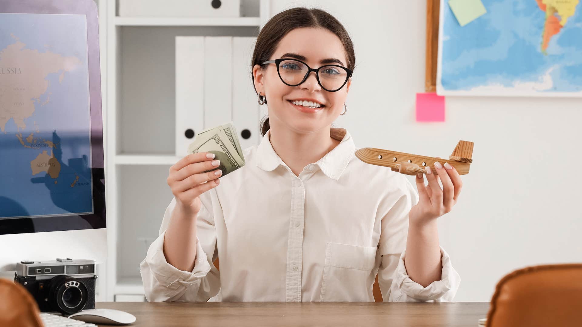 Travel agent smiling and holding money at her desk.
