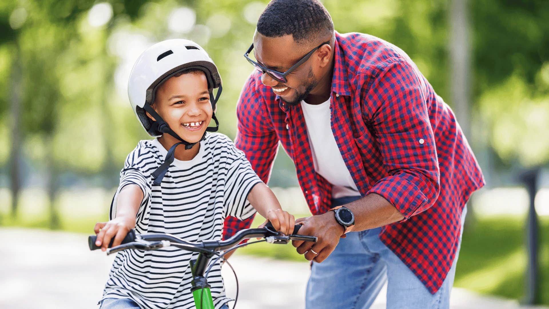 little boy learning a life skill riding a bike next to his dad