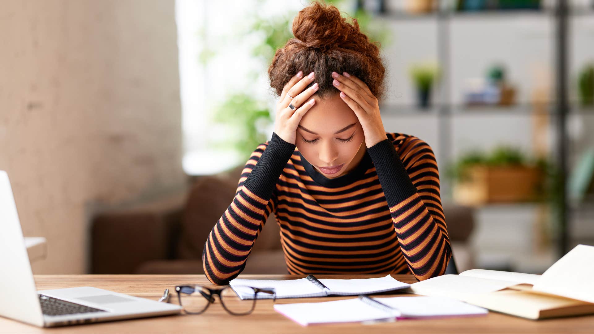 woman in stripped shirt with limited energy putting her head in hands and looking down