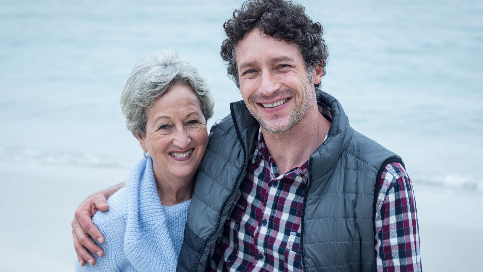 Adult son and mother who respect each other smiling and hugging at the beach.