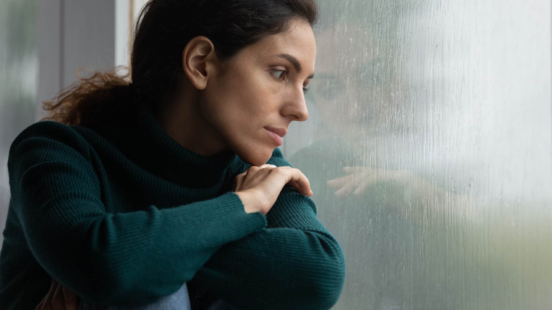 woman stares outside her window after canceling plans because of the weather