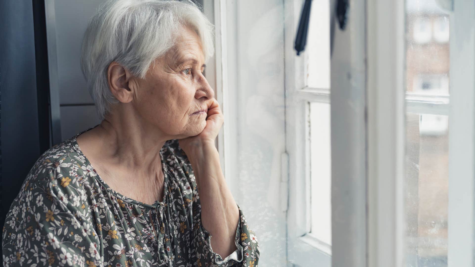 Sad older woman who's physically isolated looking out a window.