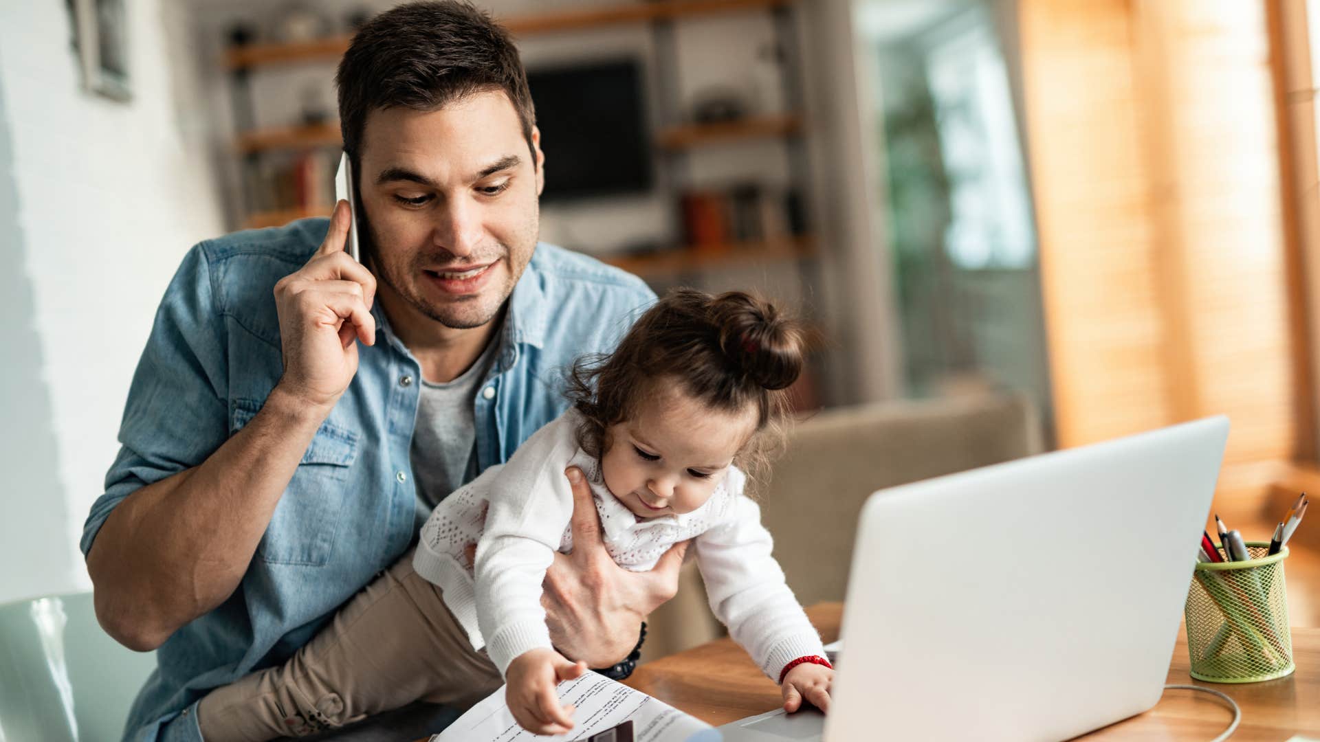 Man who's too busy with his daughter and work answering a phone call.