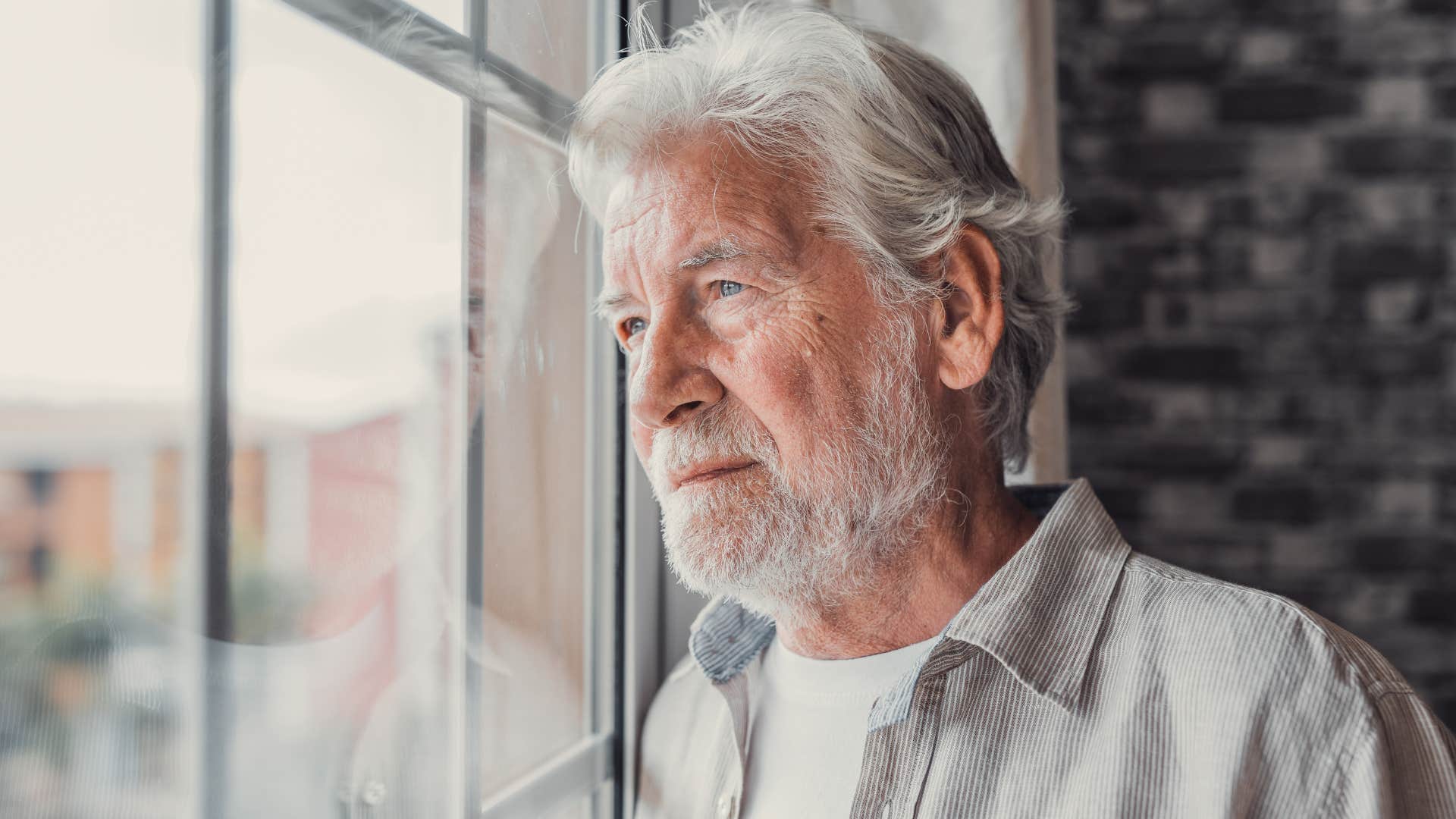 older man with unresolved trauma looking out a window
