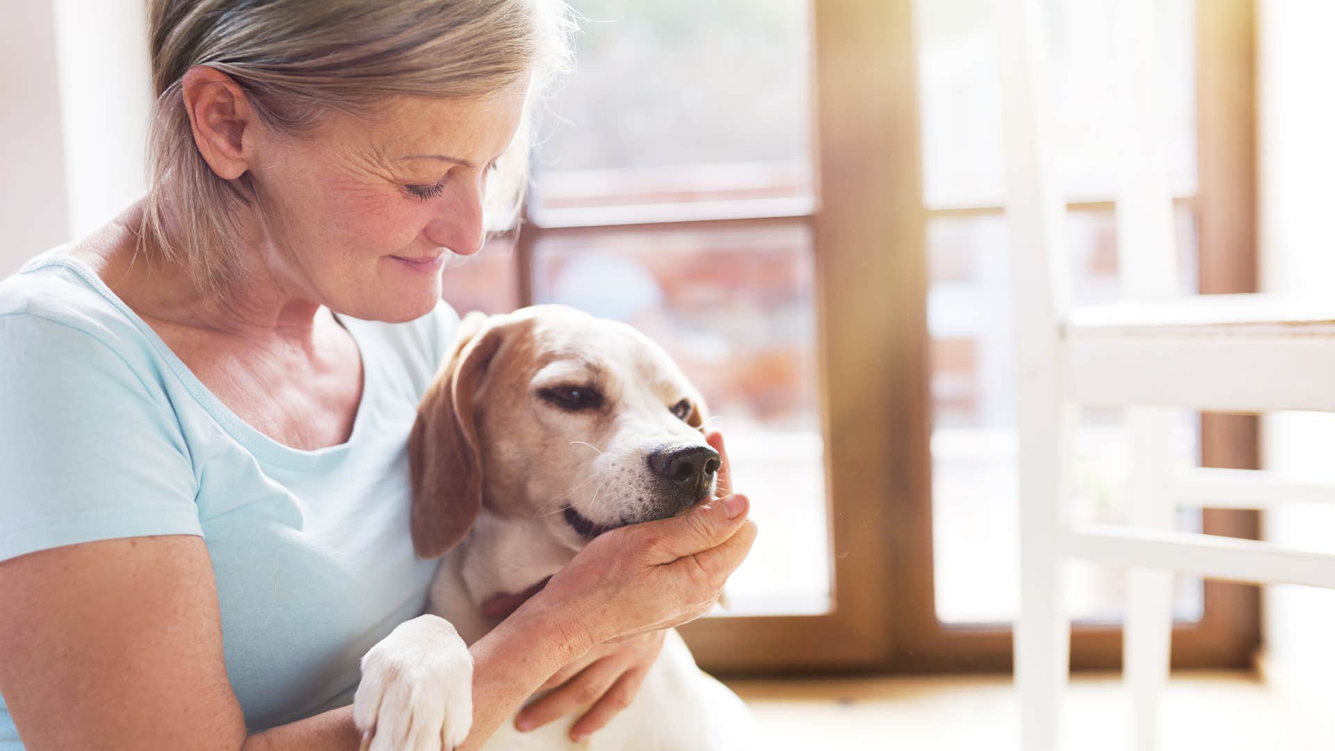 woman smiling while looking at dog licking her hand