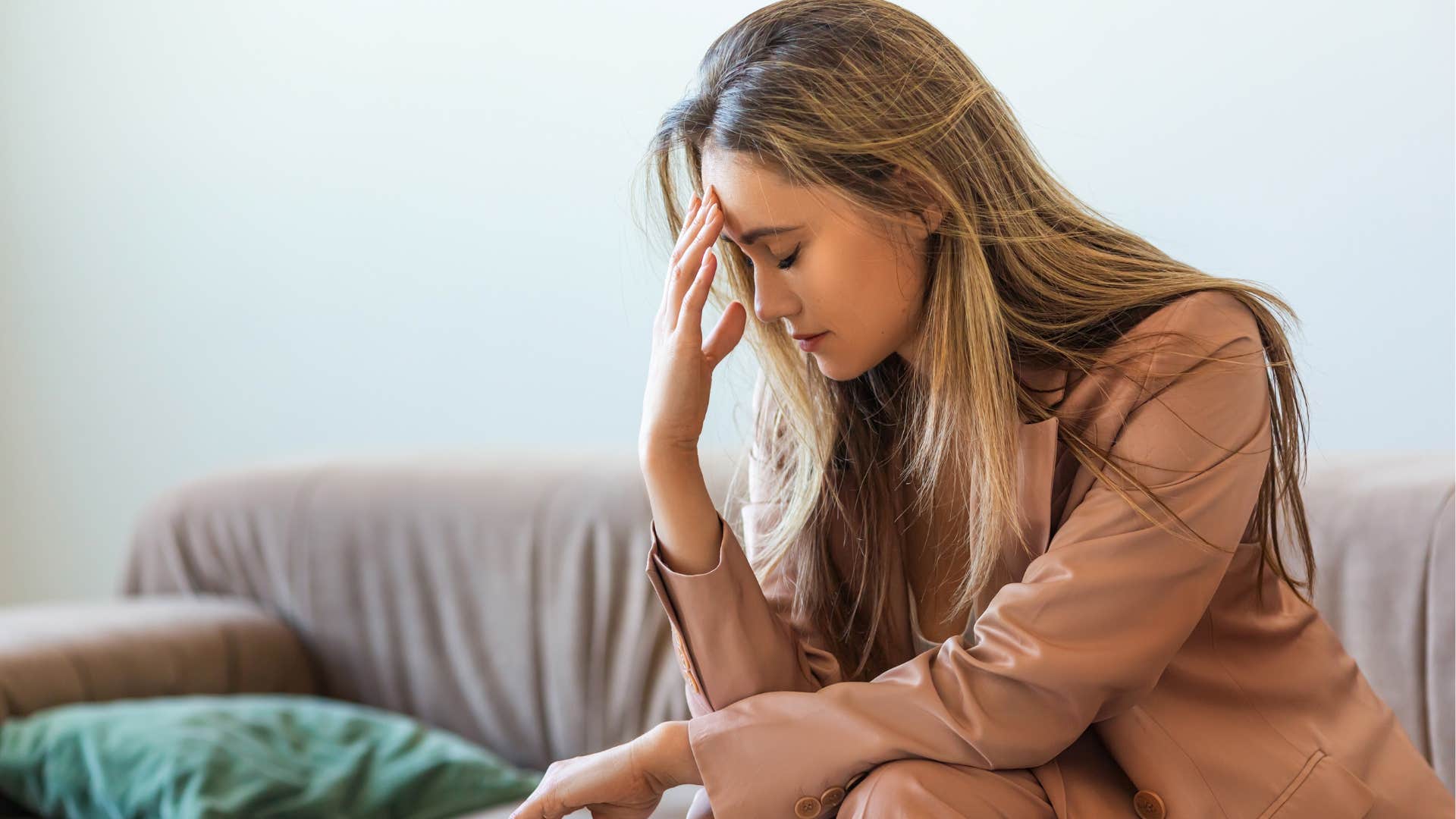 burnt out woman sitting on her couch holding her forehead