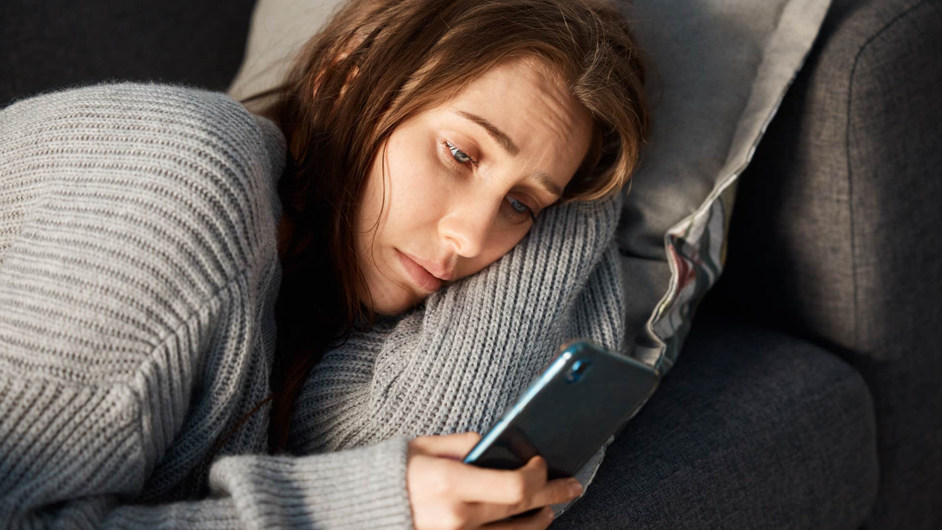 Woman who's addicted to their phone laying on the couch.