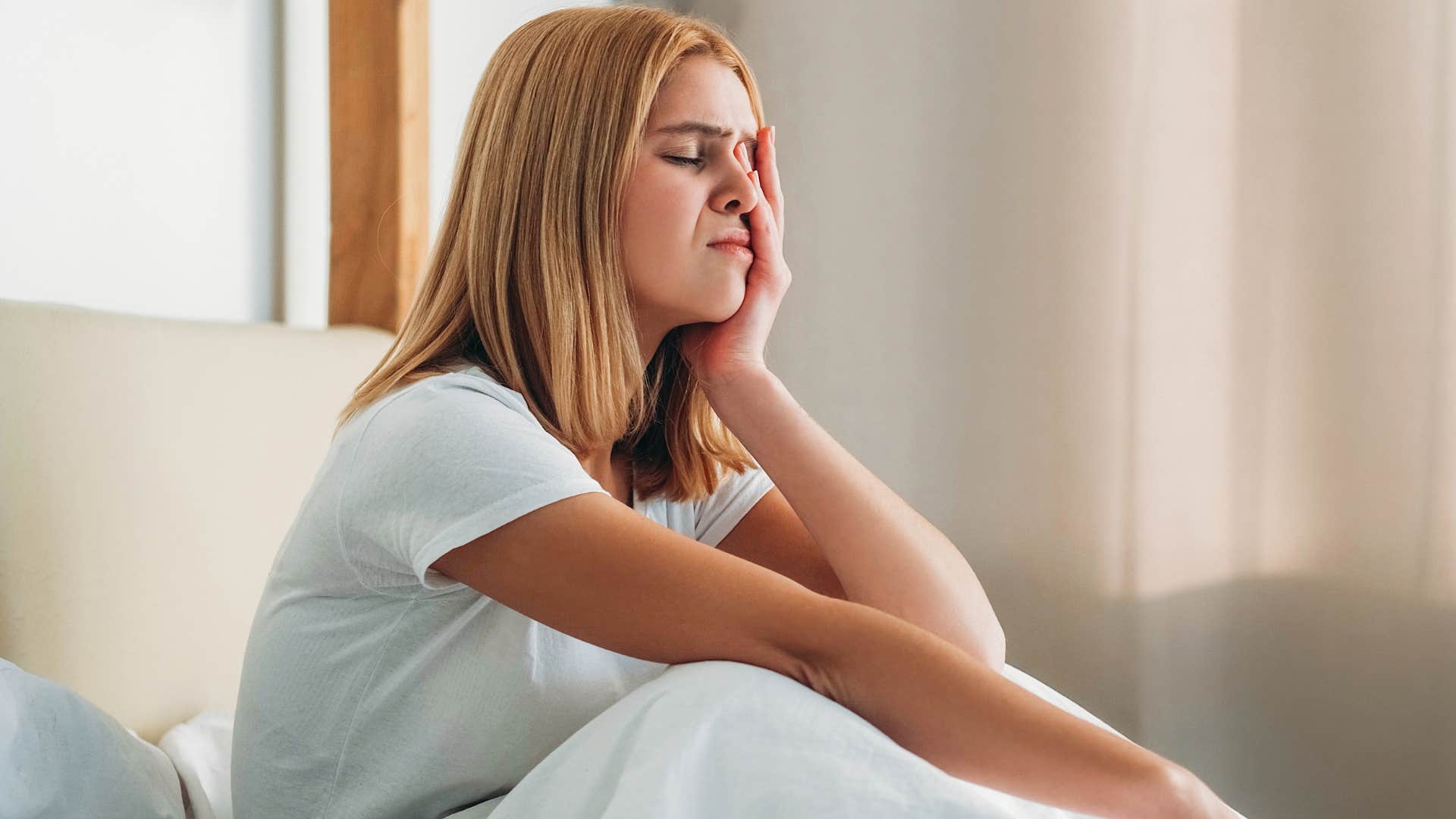 Woman with brain fog holding her head in bed.