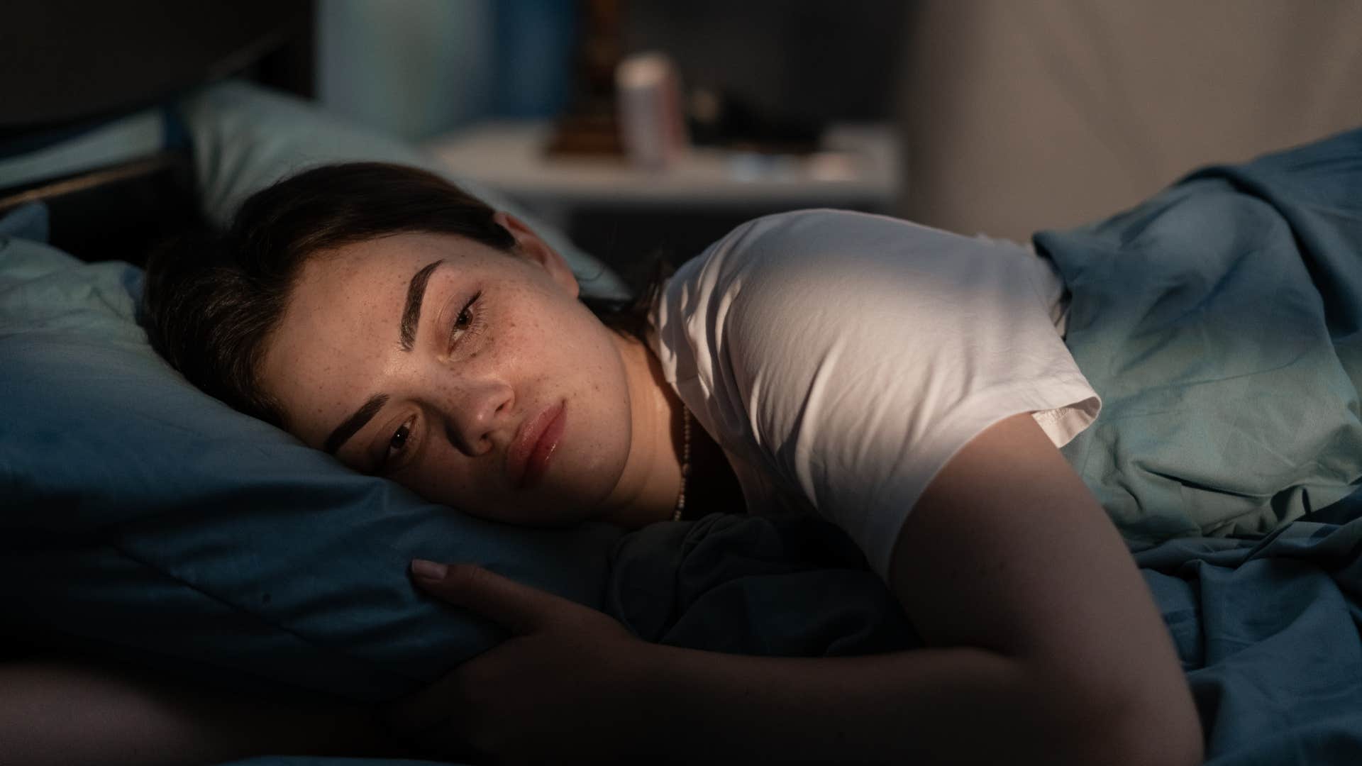 Woman struggling with insomnia laying in a dark room.
