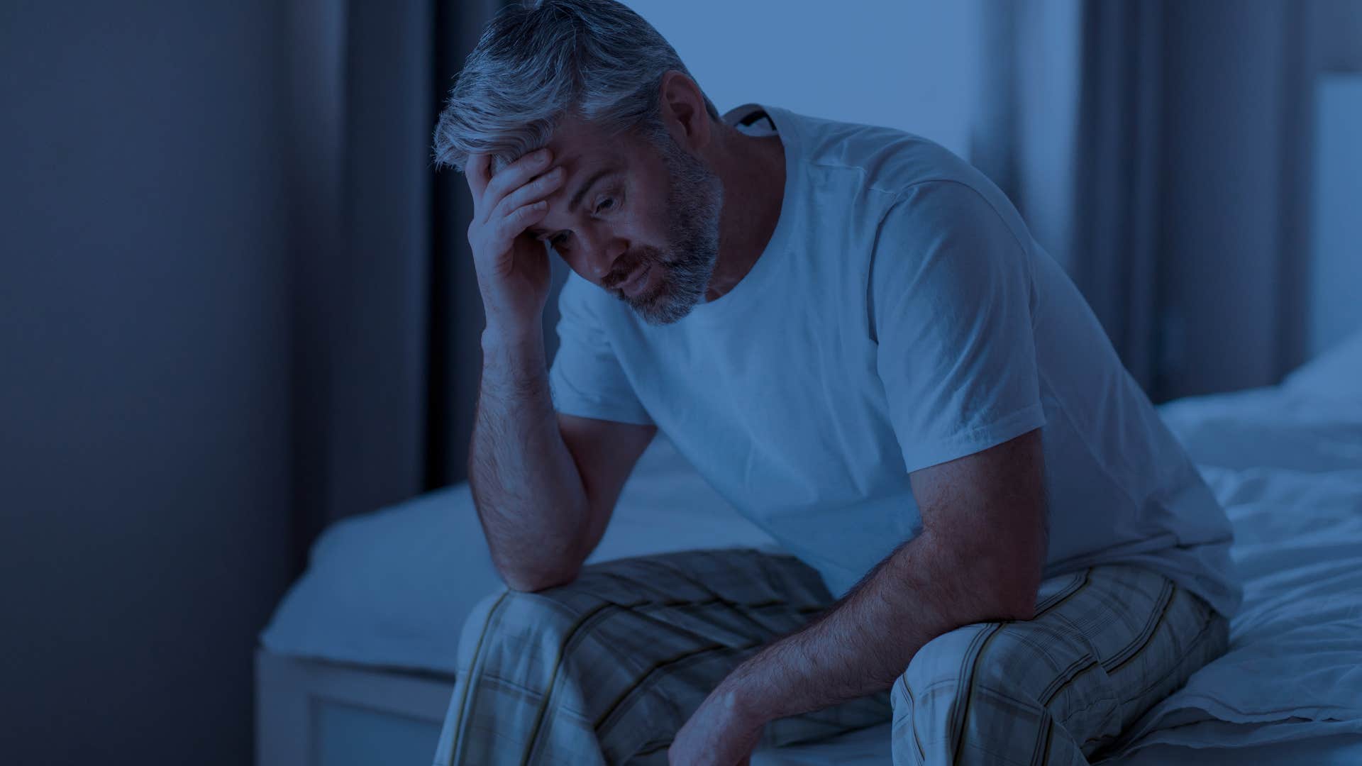 Man battling frequent nightmares holding his head in a dark room.