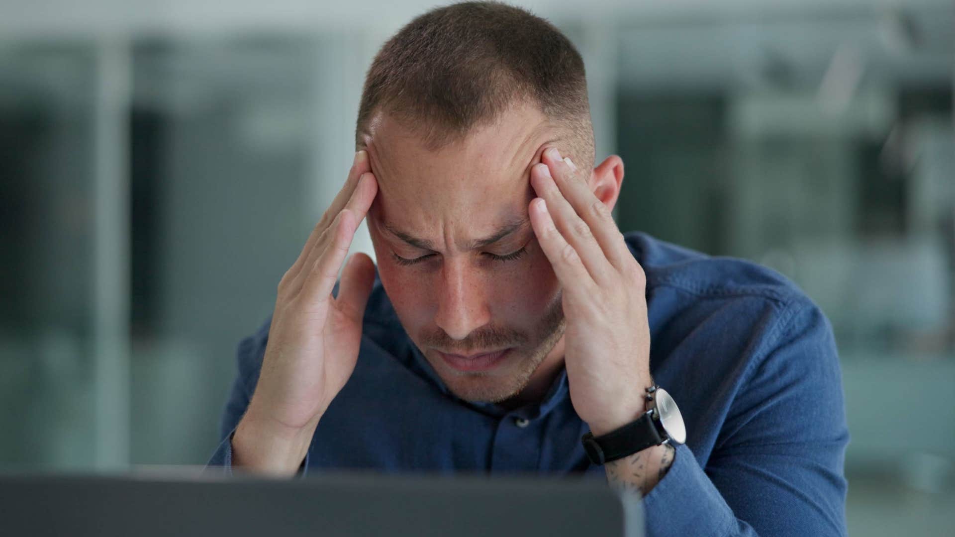Man who wakes up tired holding his head at work.