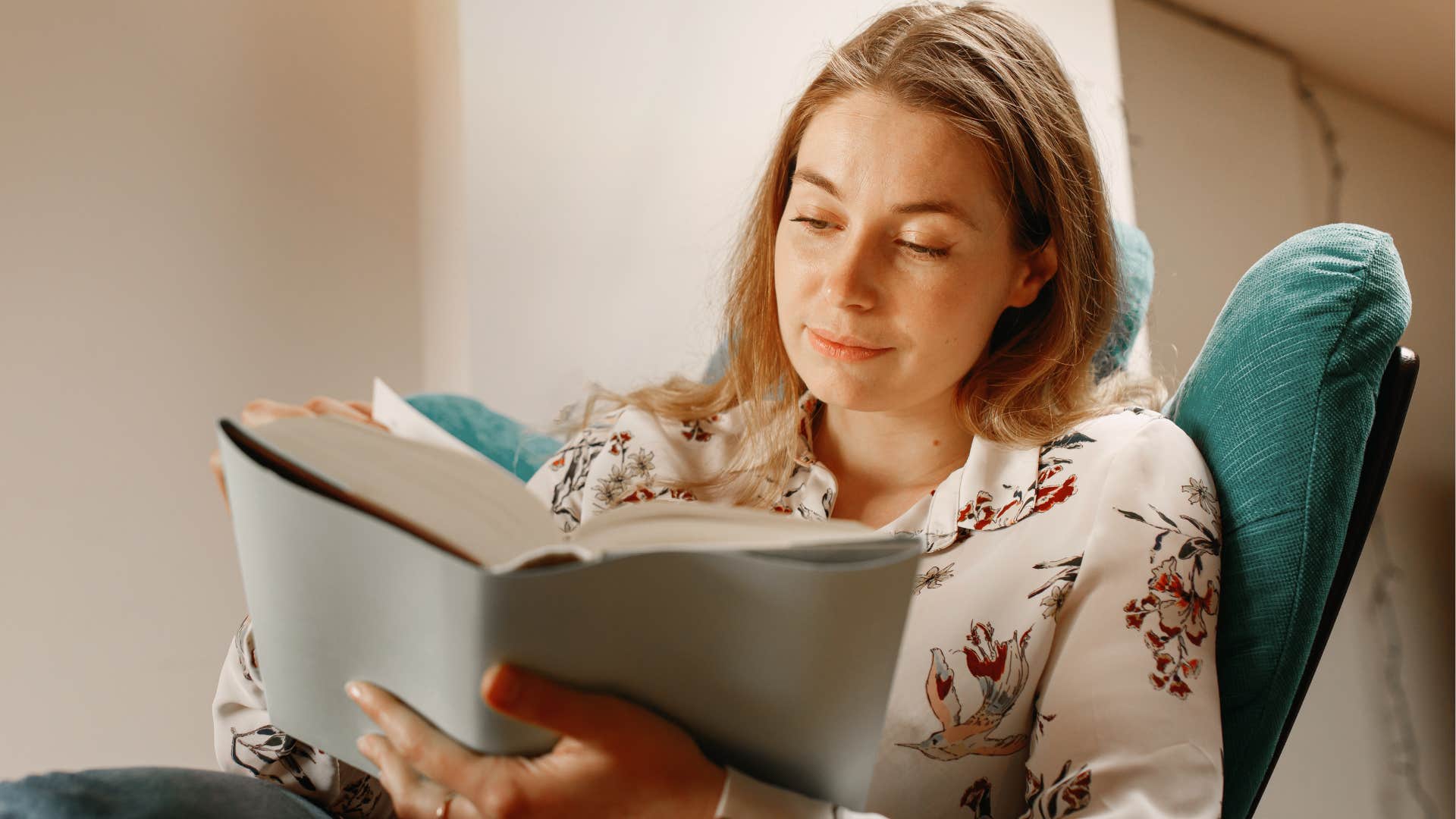 Woman with lots of books reading in a chair at home.