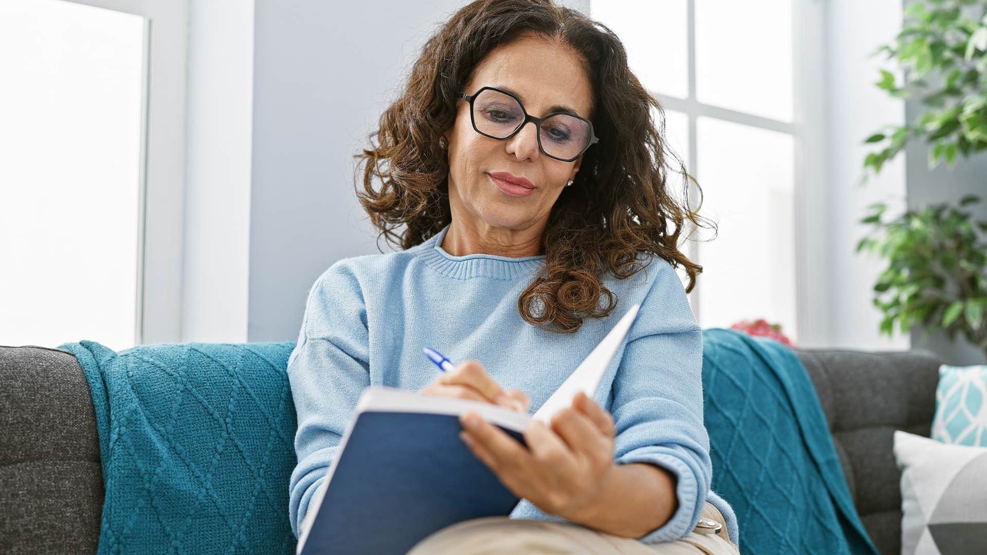Woman smiling and writing in her journal on a couch.