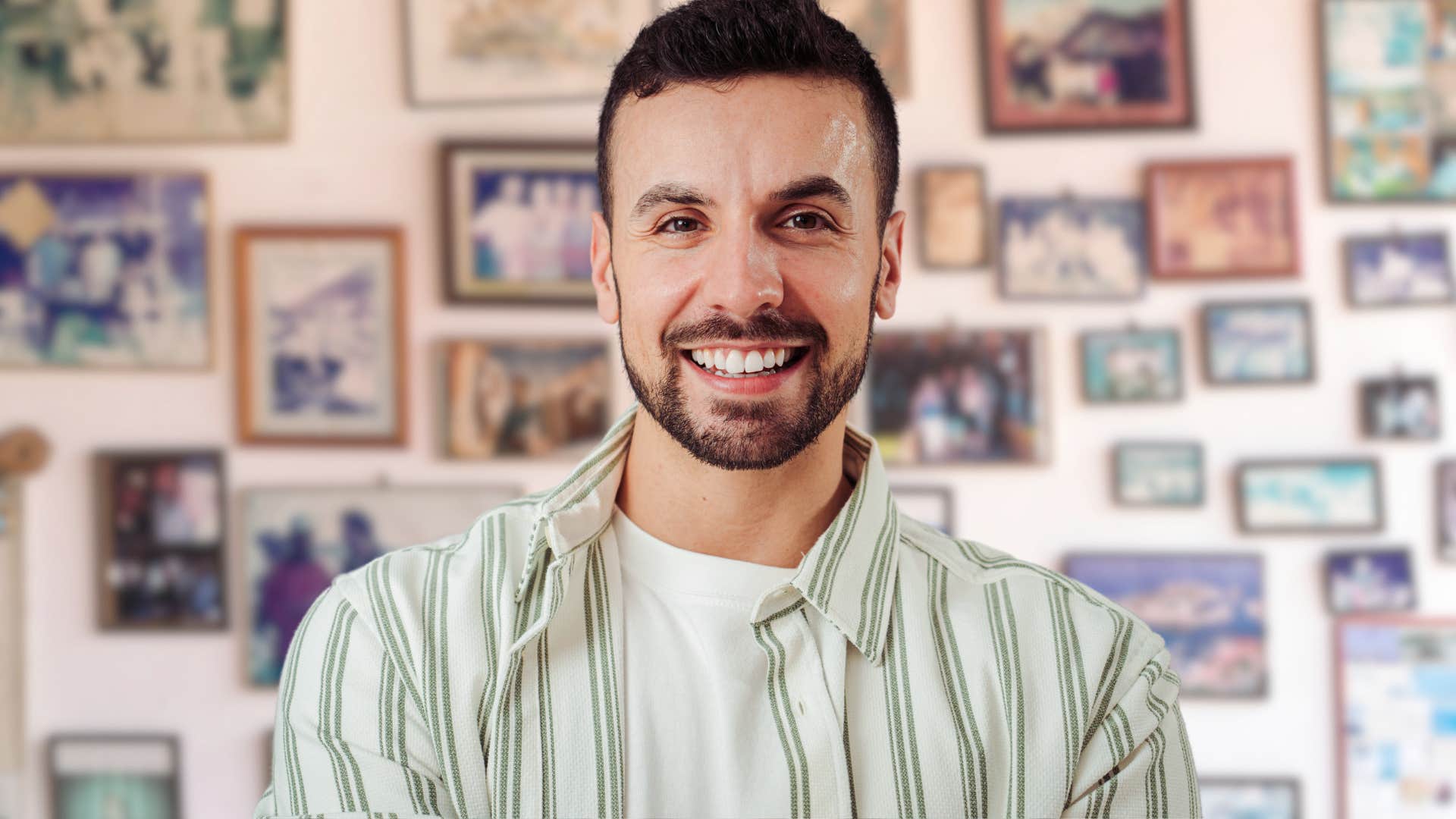 Man smiling in front of a wall of sentimental photos.