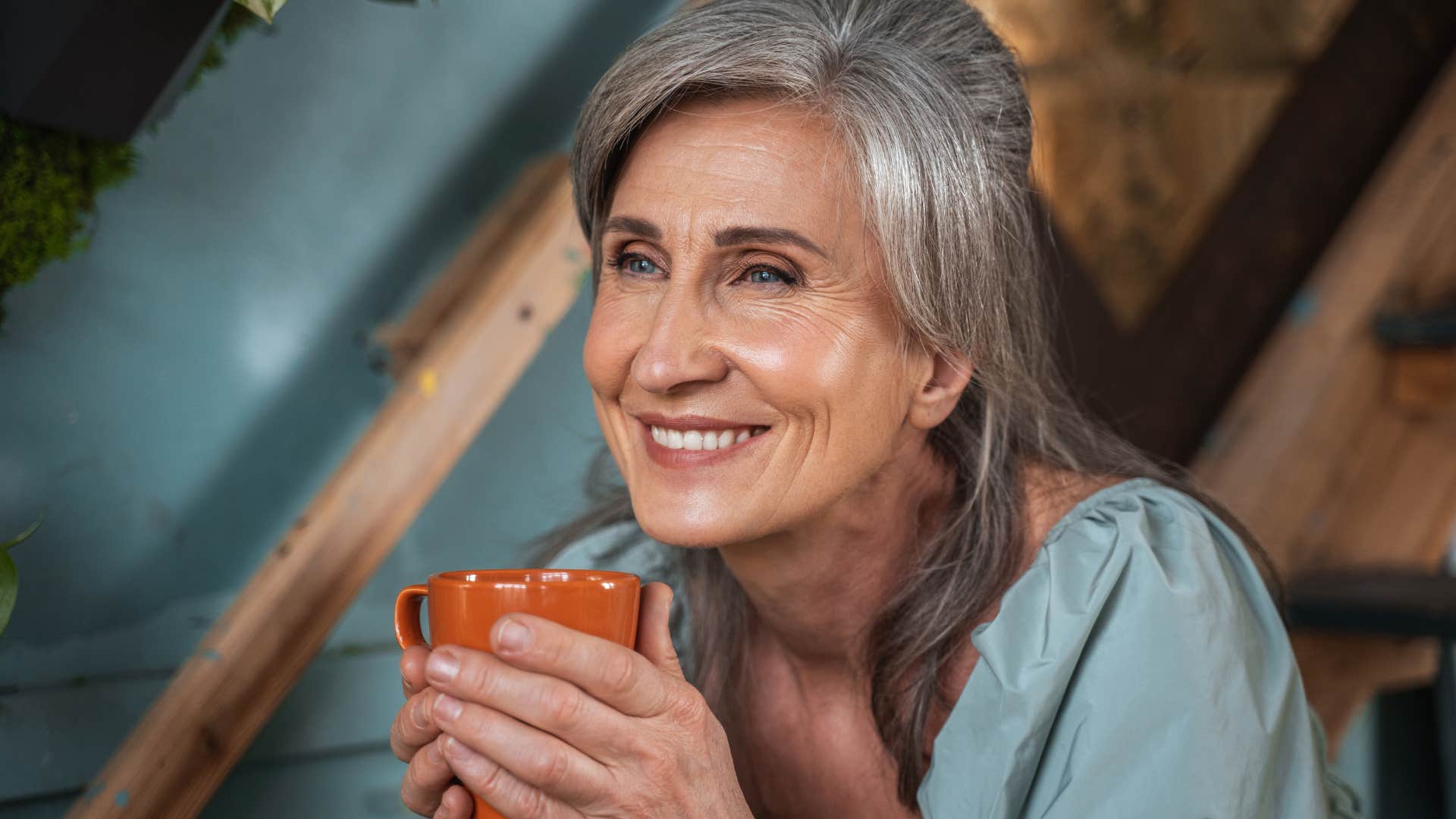 Older woman smiling and sitting in her safe space with a cup of coffee.