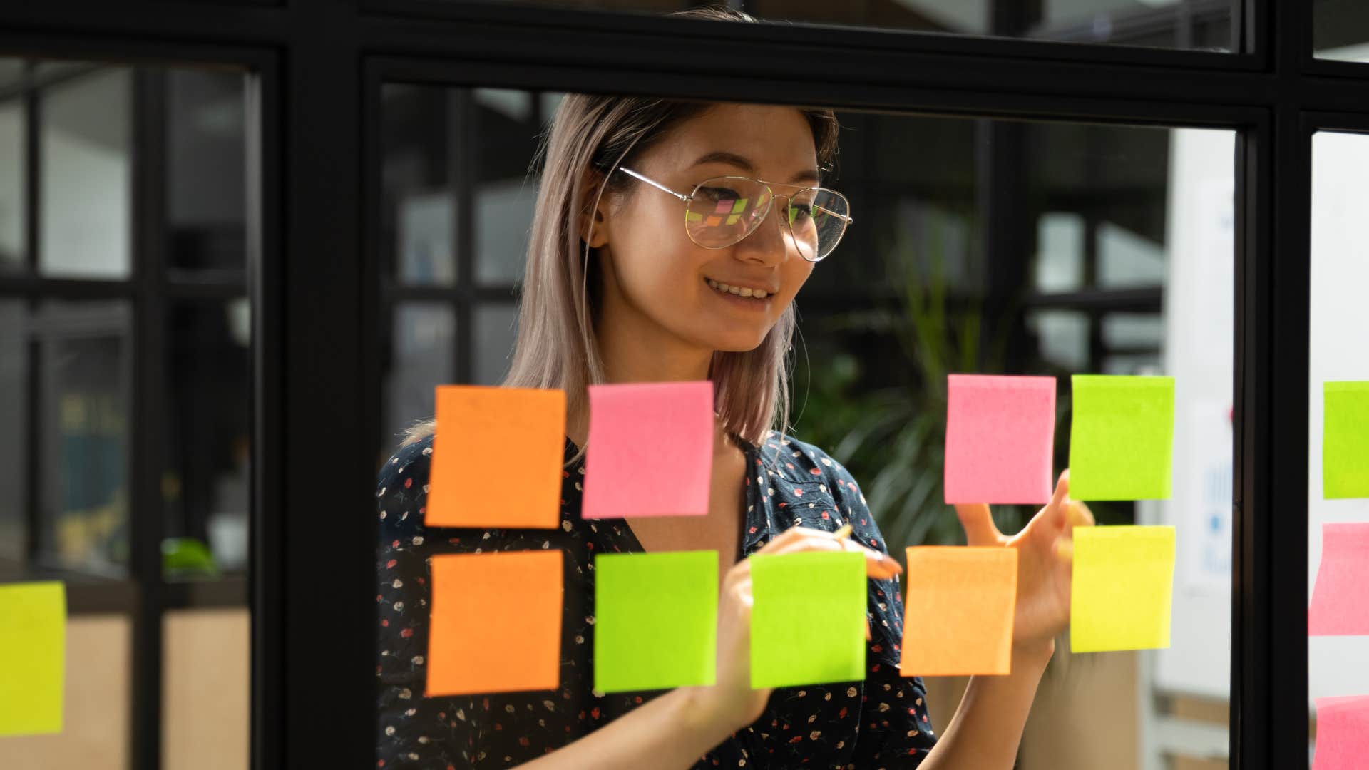 Woman smiling and putting up sticky notes on a wall.